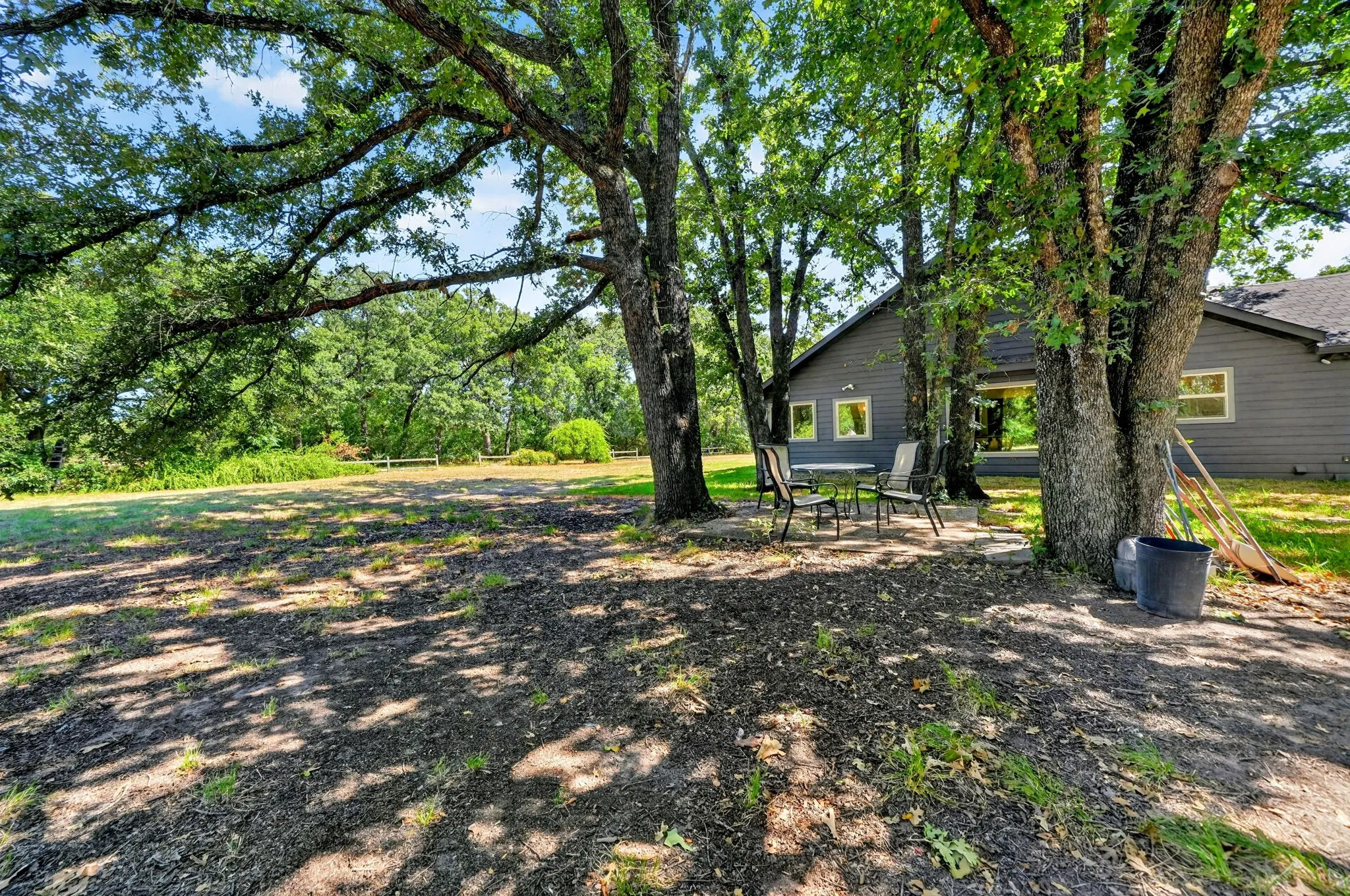 Mature shade trees frame this expansive outdoor living space, offering natural canopy coverage over the grounds