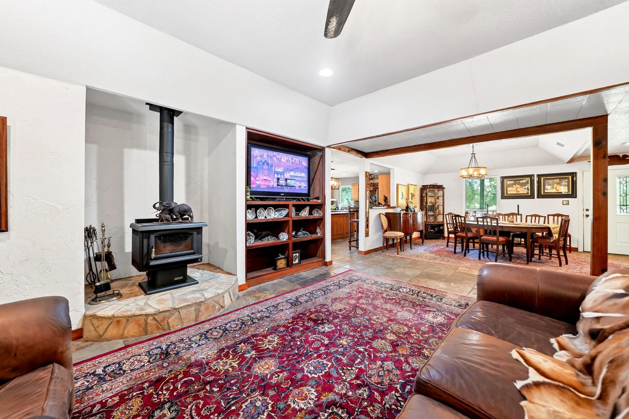 Spacious open-concept living area anchored by a wood-burning stove with decorative surround, complemented by rich wood-finish flooring and an ornate area rug