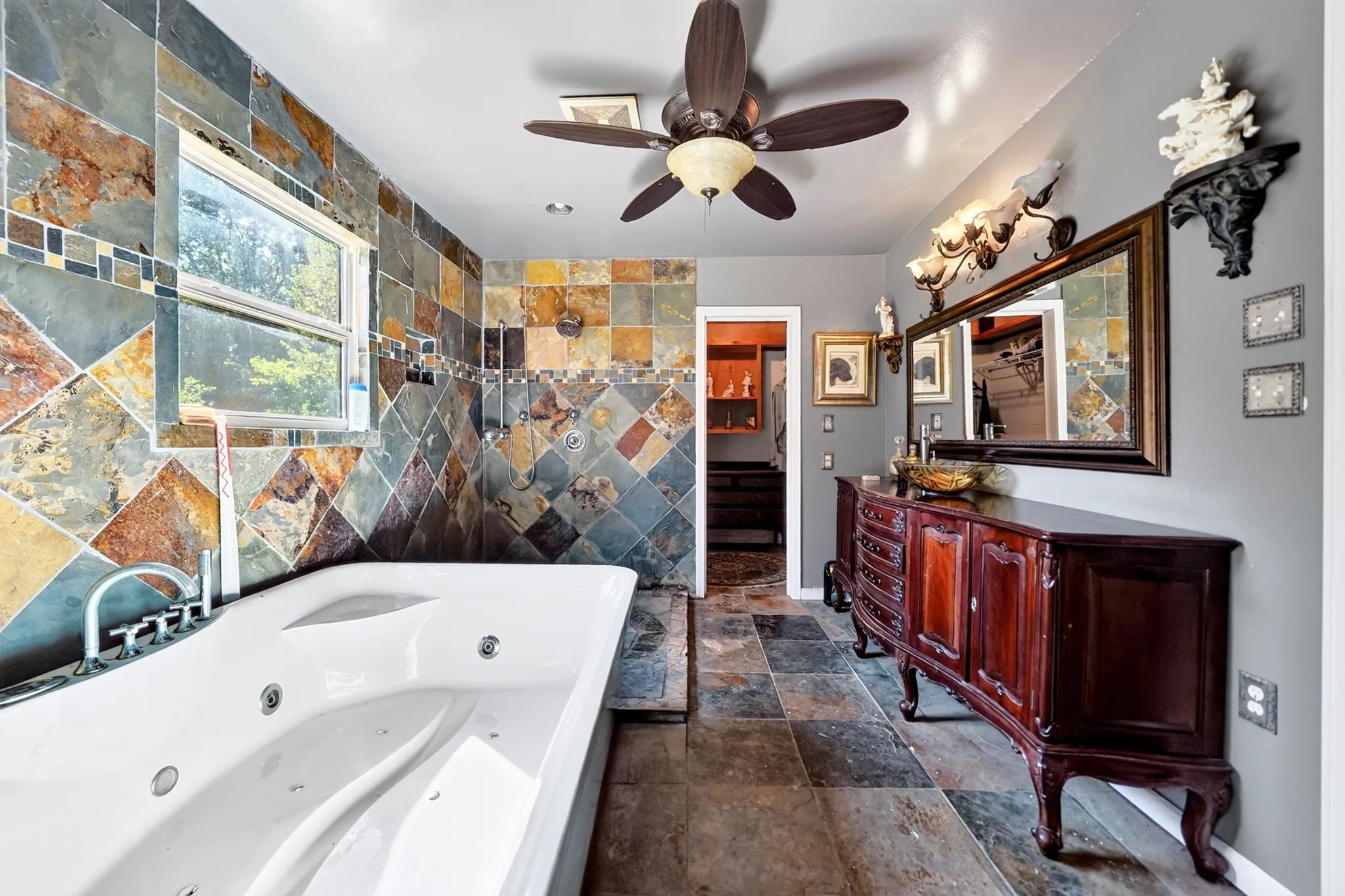 Jetted soaking tub with chrome fixtures, multi-toned tiled shower surround, coordinated tiled flooring, and a ceiling fan with integrated lighting