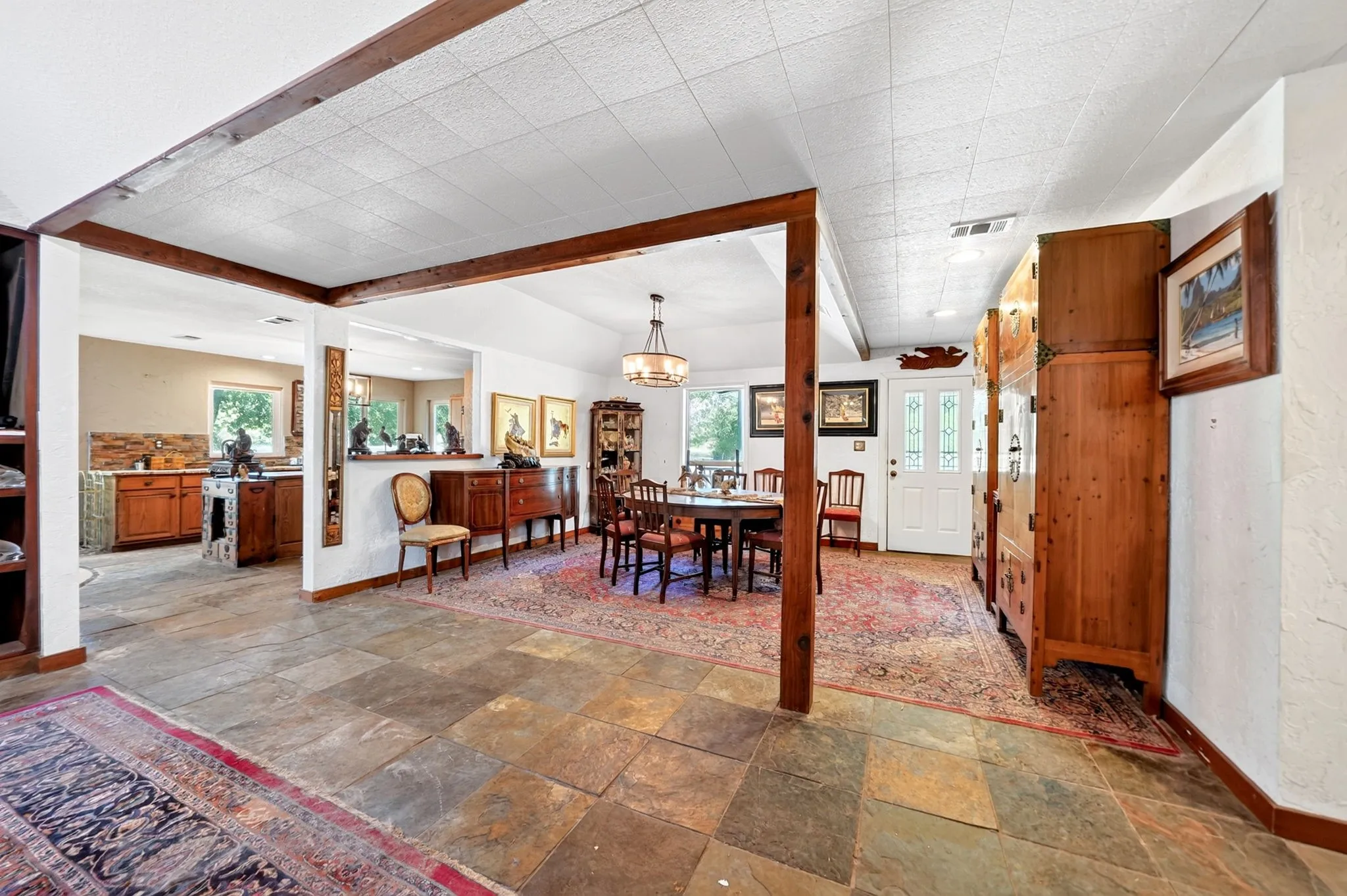 Spacious open-concept living area featuring exposed wood beam supports, slate-finish flooring with geometric patterning, and abundant natural light from multiple windows