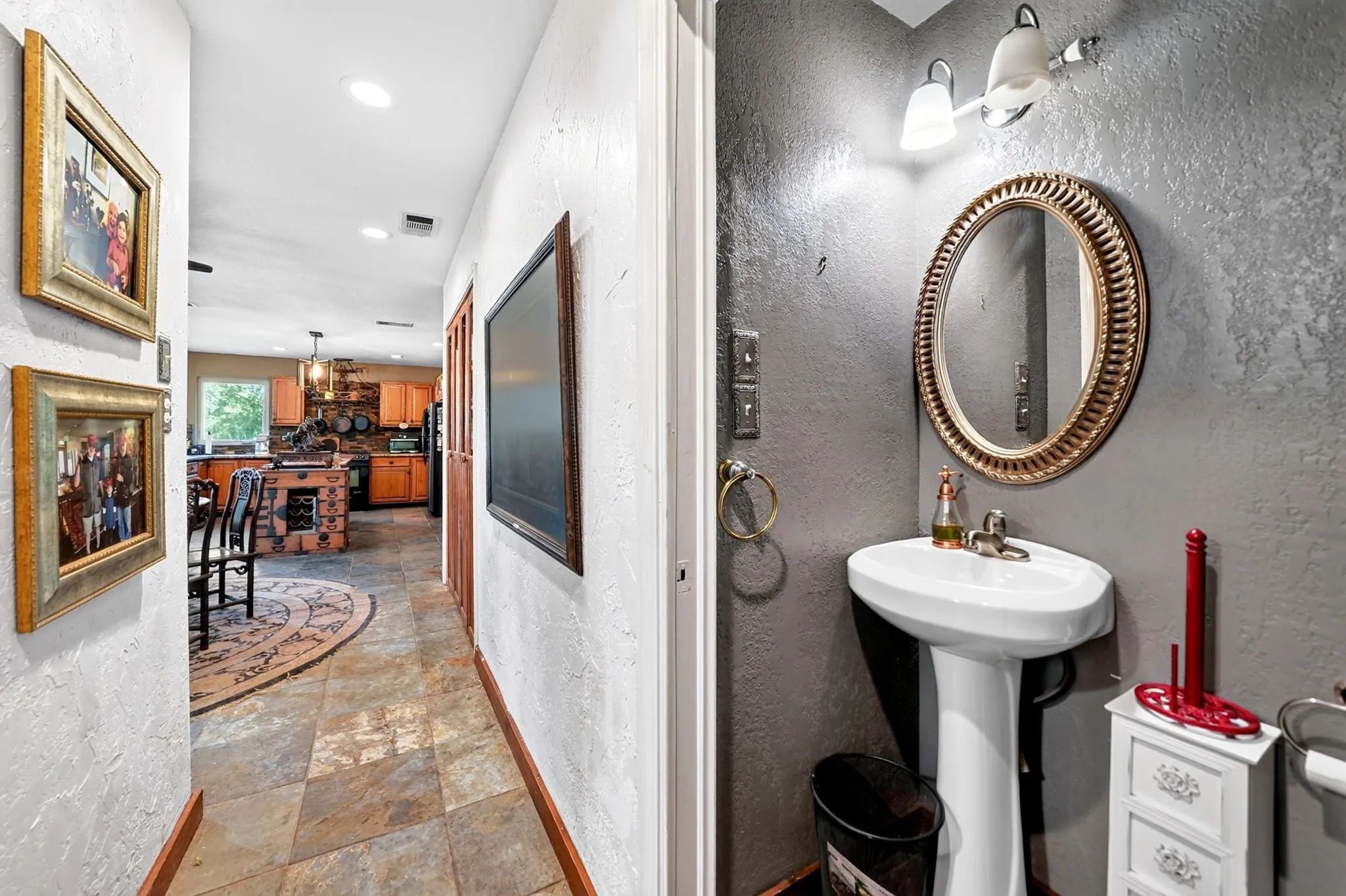 Hallway and powder room featuring tile flooring, an oval framed mirror, pedestal sink with chrome fixtures, and recessed lighting throughout