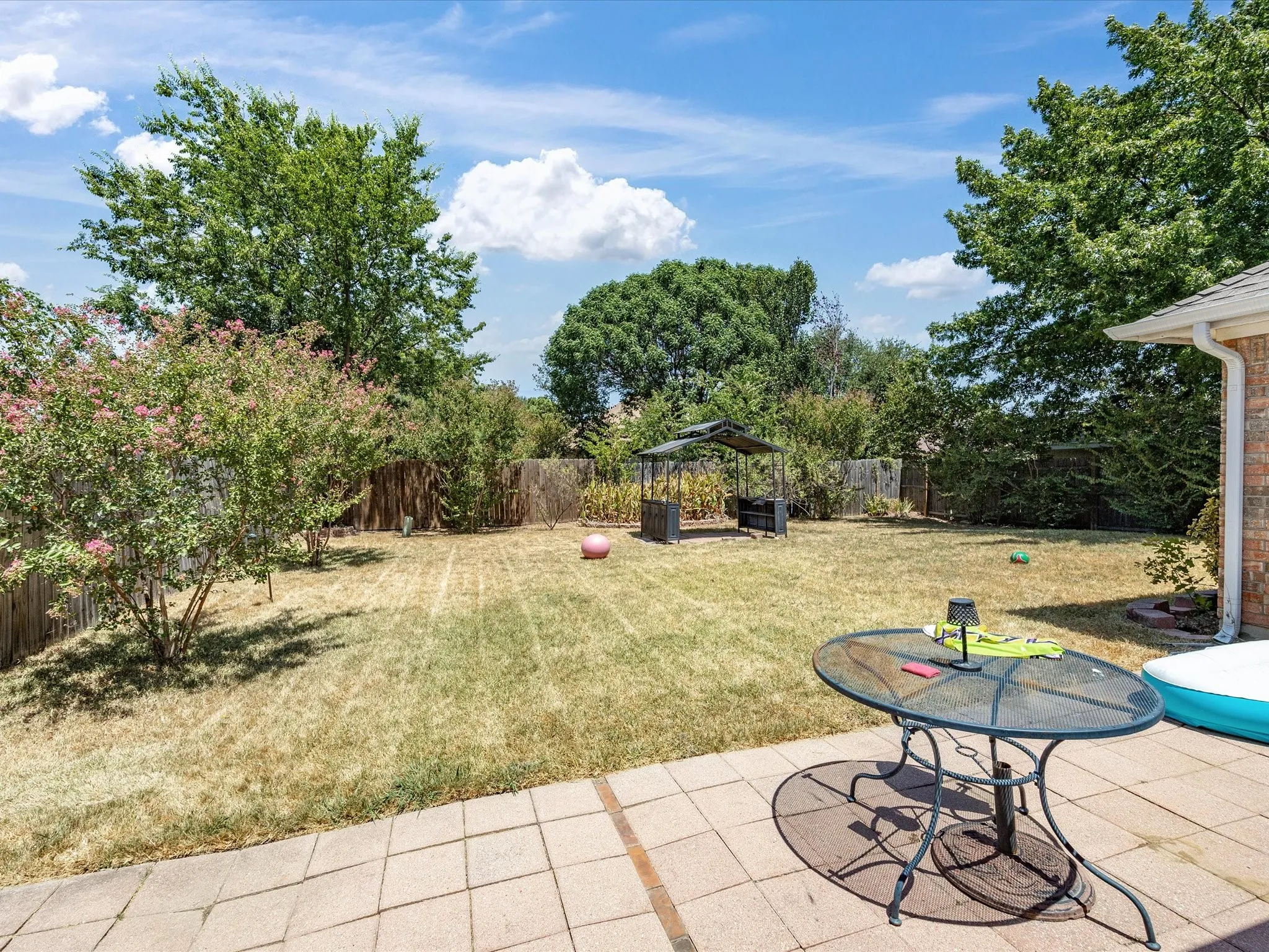 Expansive backyard oasis featuring mature landscaping, a manicured lawn, fenced perimeter, patio with tile hardscaping, and a resort-style pool with integrated spa—ideal for outdoor entertaining and recreation