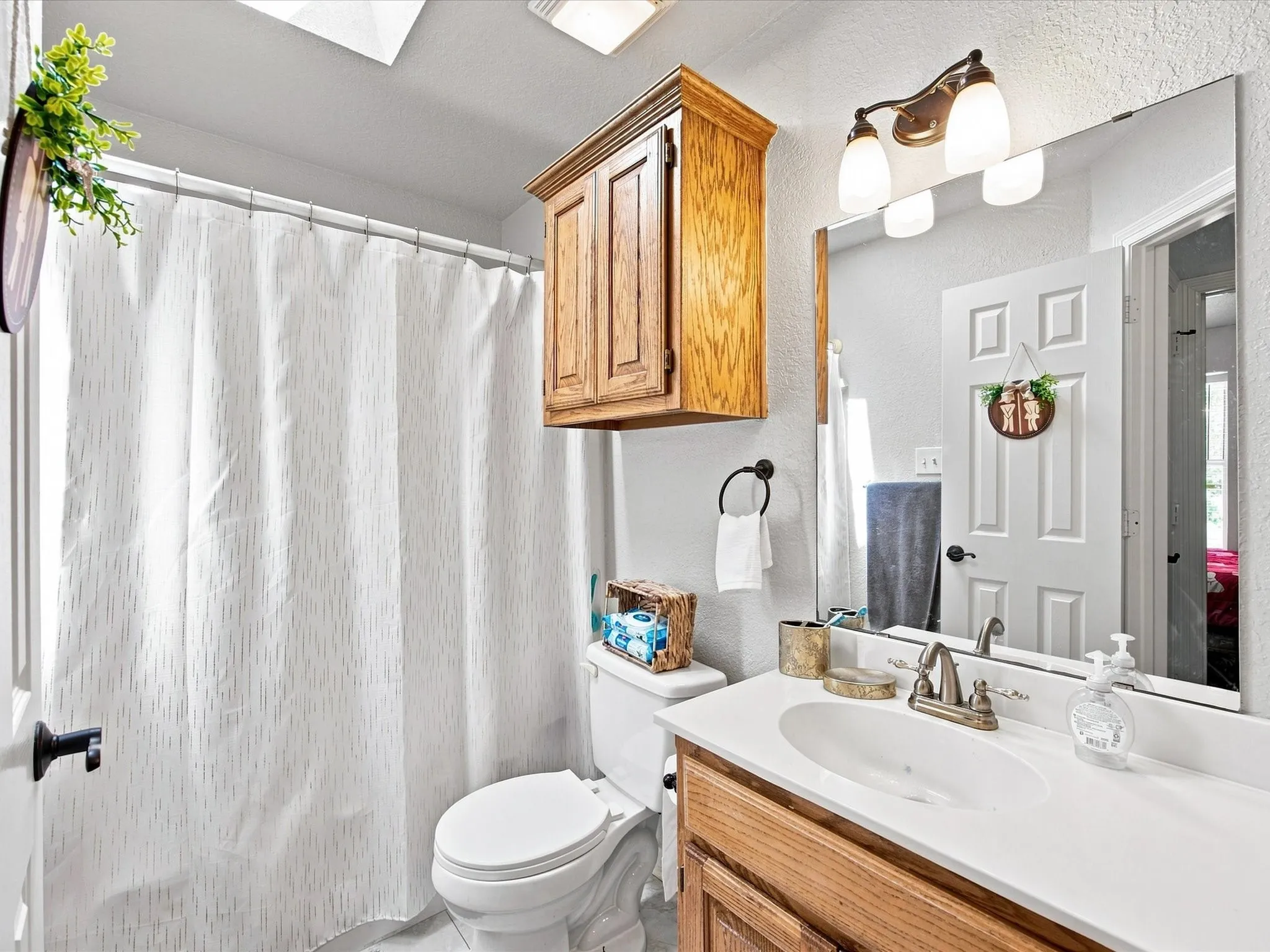 Spa-inspired bathroom featuring warm wood cabinetry with dual-sink vanity, white quartz countertop, brushed nickel fixtures, and ample storage with overhead wooden cabinet