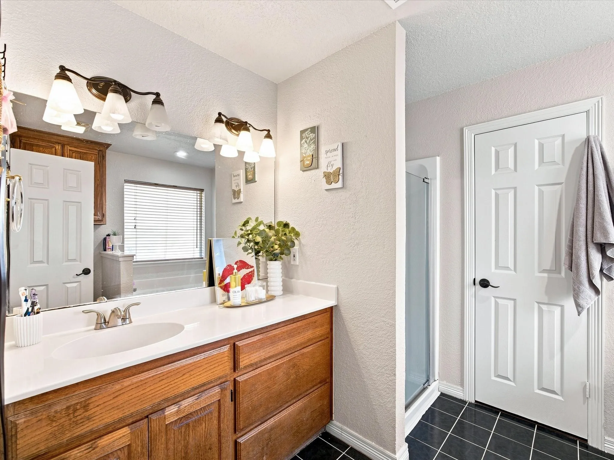 Master bathroom featuring dual vanity with wood-finish cabinetry, white quartz countertop, chrome fixtures, and contemporary bronze-finish lighting