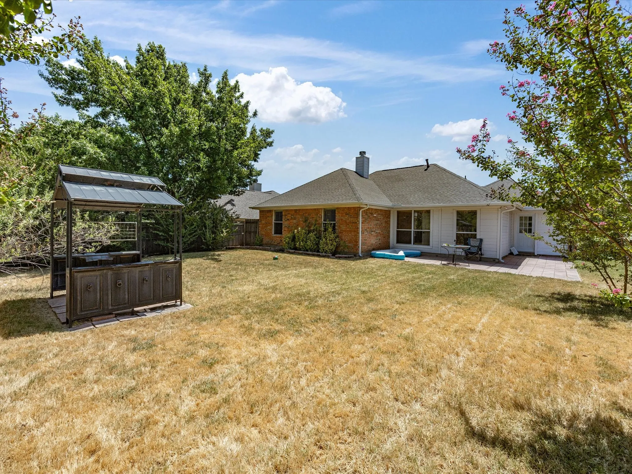 Expansive backyard with a dedicated grilling station, mature perimeter landscaping, and a paver patio