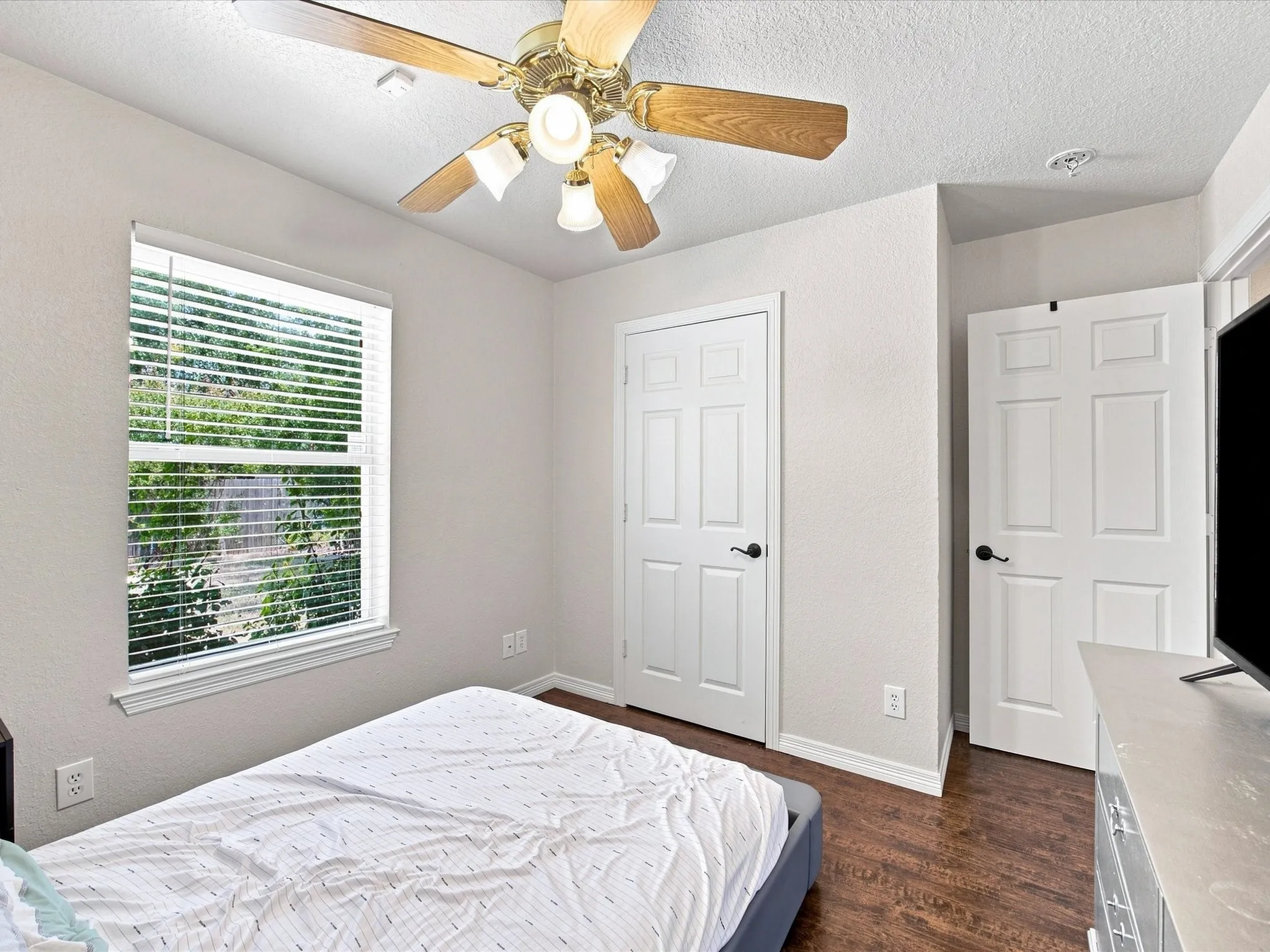Spacious bedroom featuring wood-finish flooring, a ceiling fan with integrated lighting, and dual closet doors