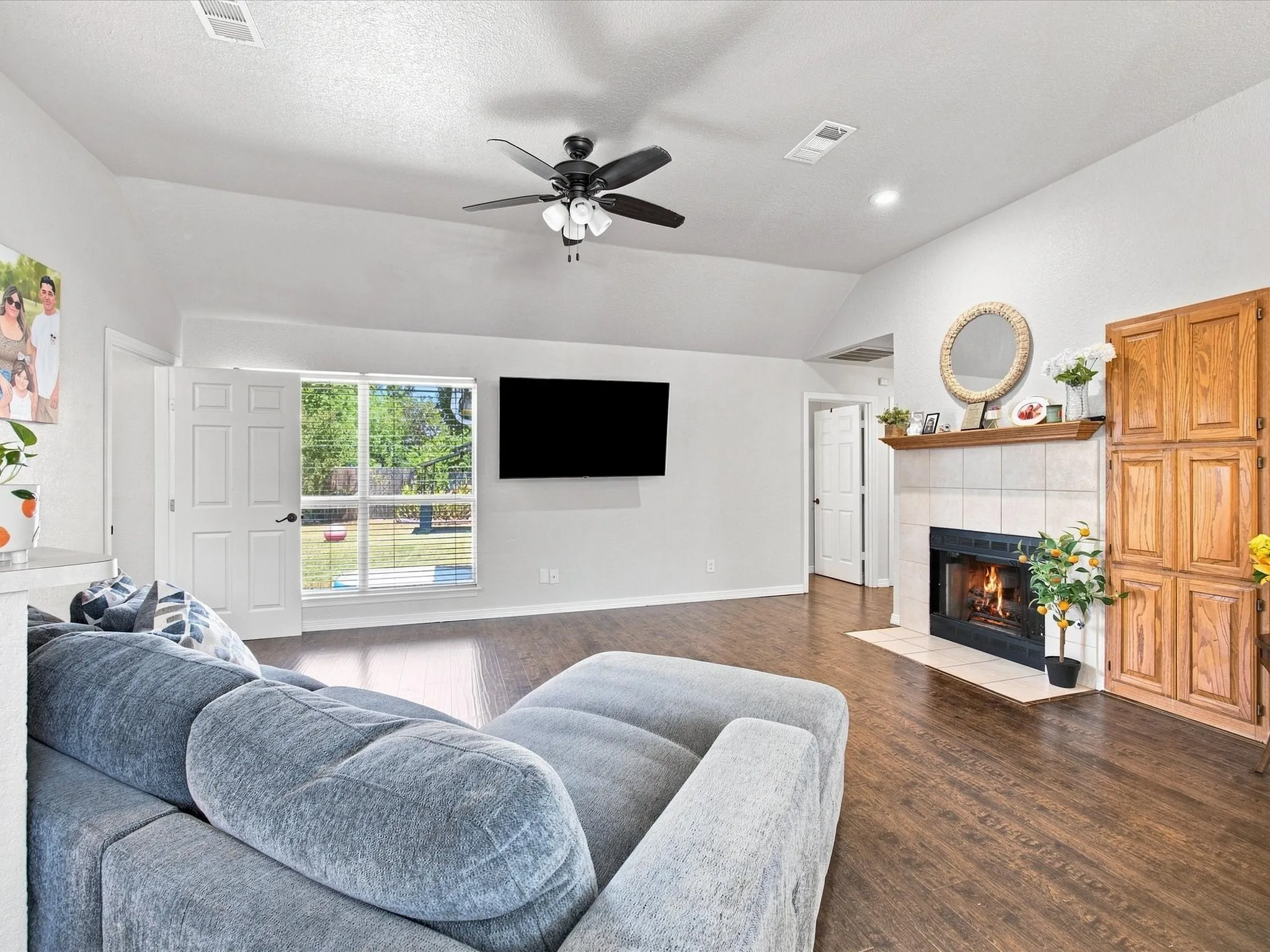 Spacious living room featuring hardwood flooring, a ceiling fan with integrated lighting, a wall-mounted flat-screen television, and a gas fireplace with built-in cabinetry