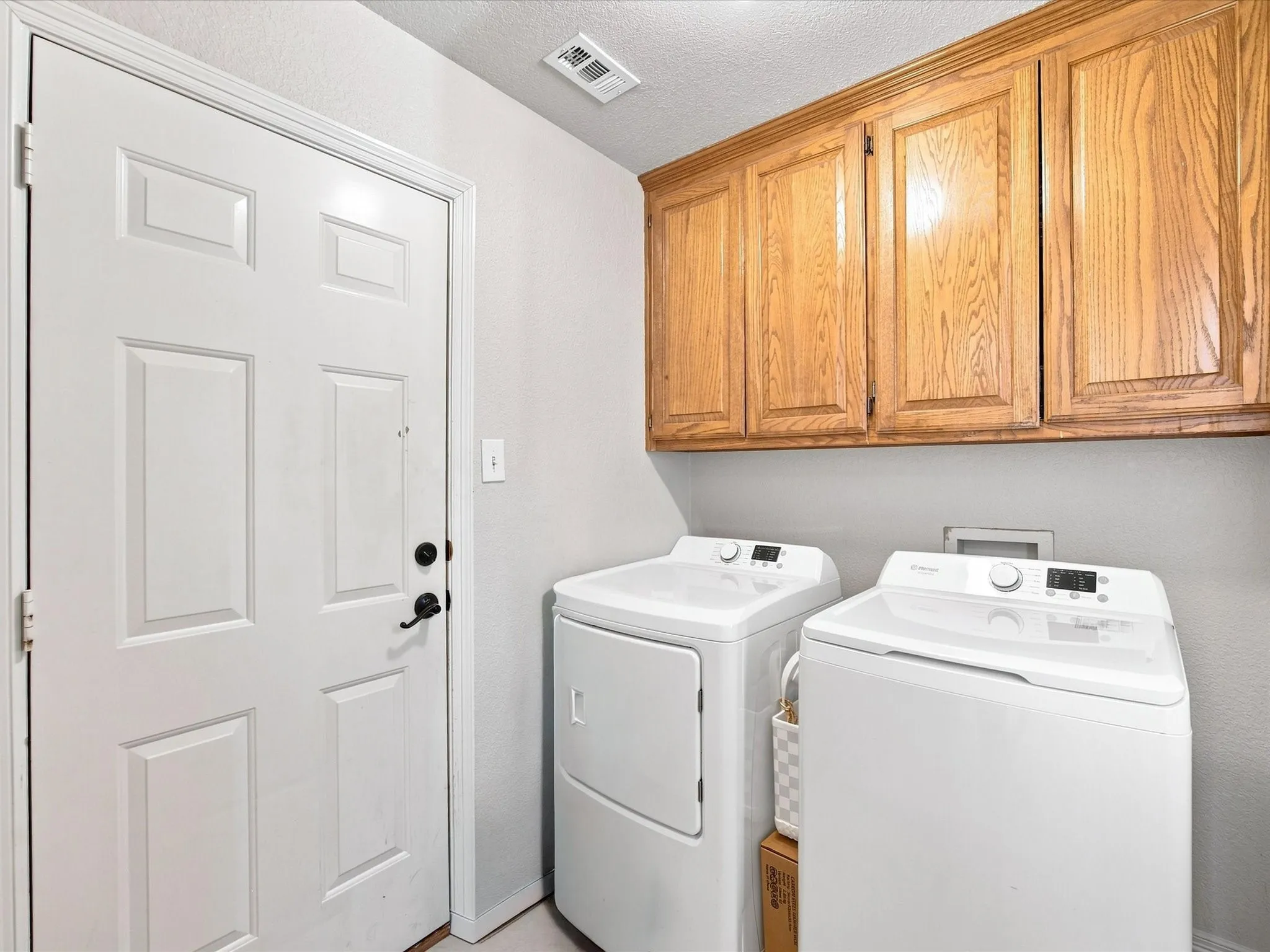 Laundry area featuring overhead wood cabinetry and a paneled door with black hardware
