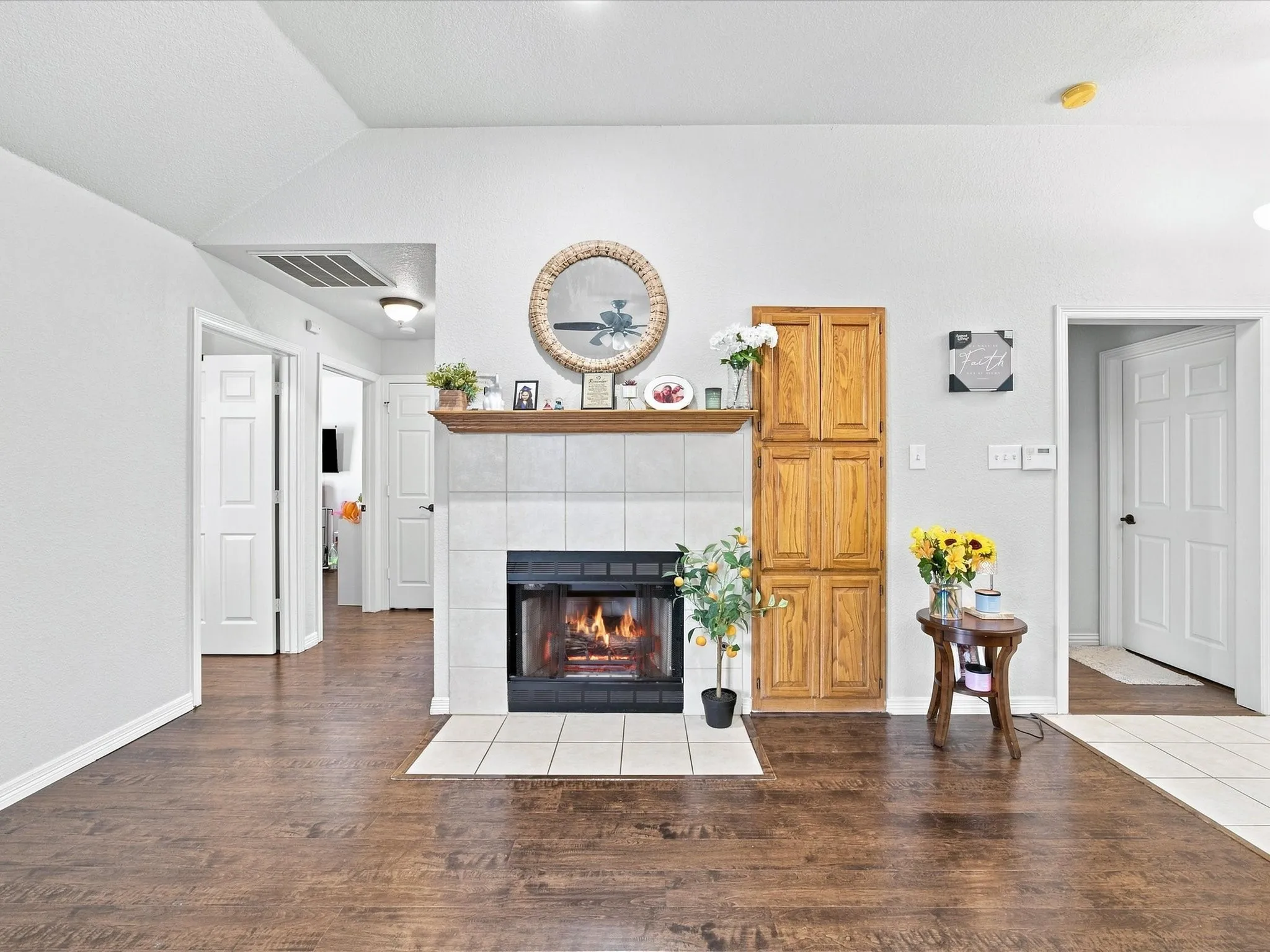 Vaulted ceiling with recessed lighting, wood-finish flooring, tile-surround fireplace with mantel, and built-in wood cabinetry