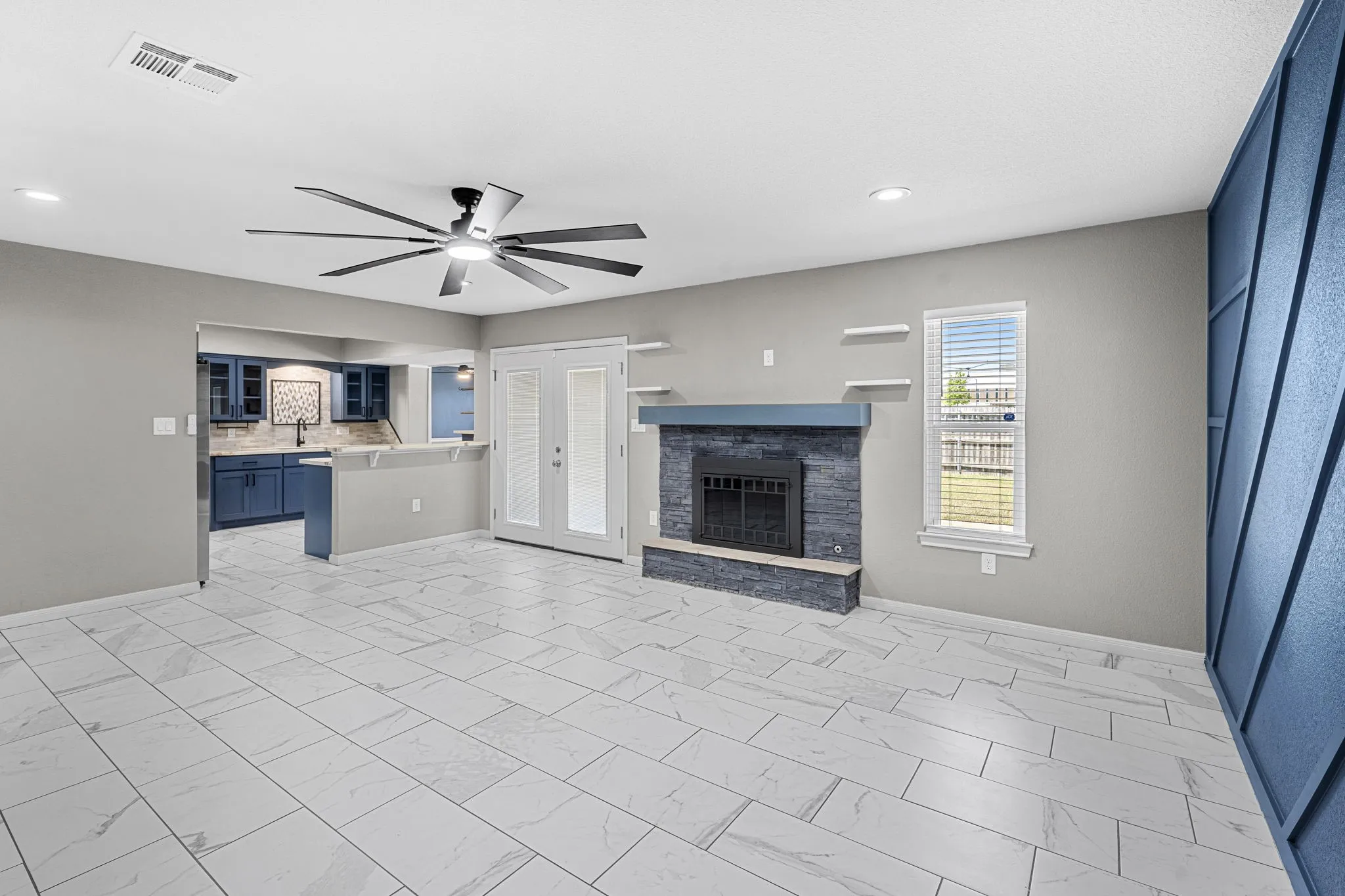 Open-concept living space with large format tile flooring, a fireplace featuring a stone surround and hearth, and a modern ceiling fan