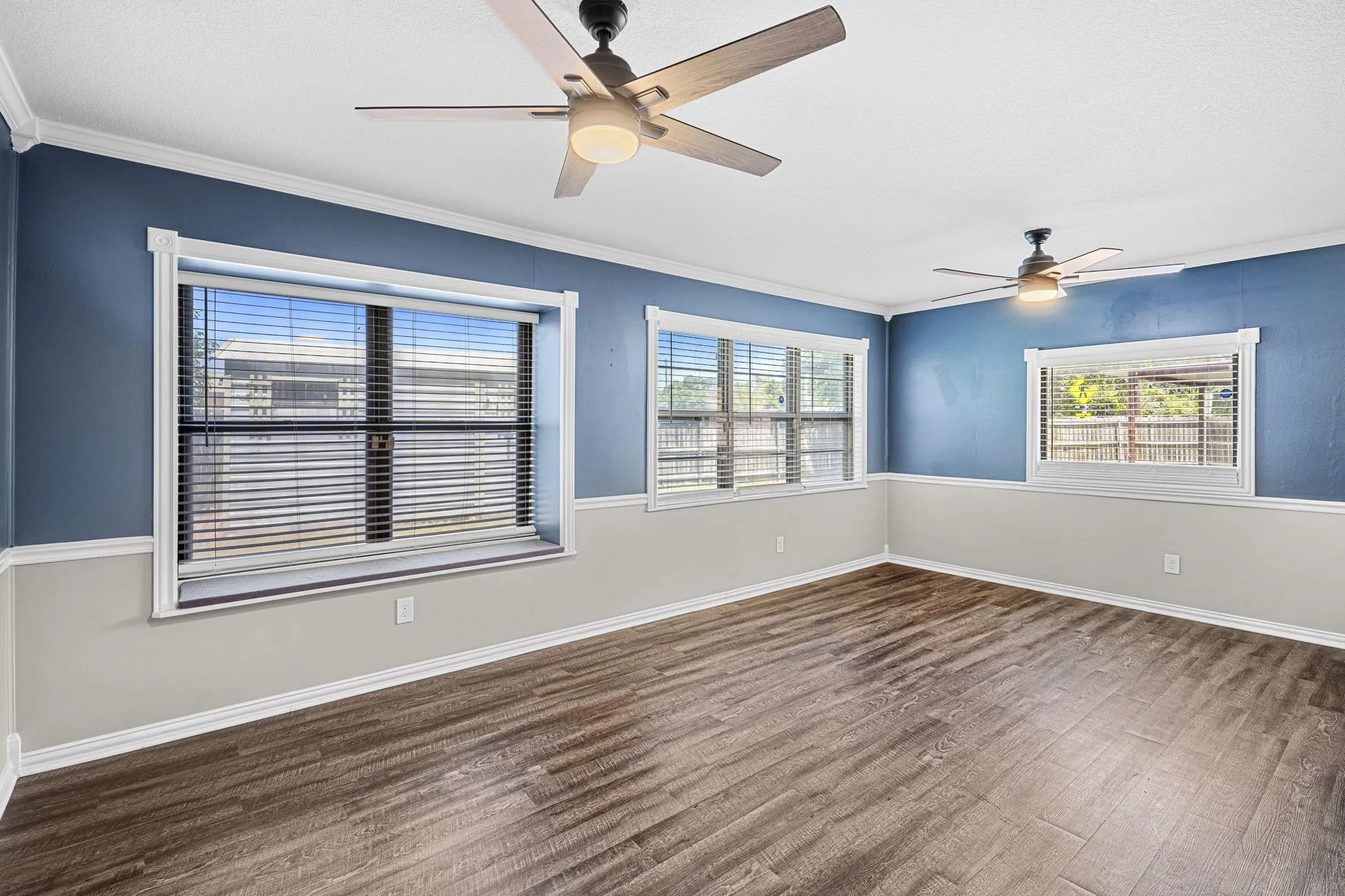 Wood-finish flooring, multiple windows, two ceiling fans with integrated lighting, and two-tone wall treatment