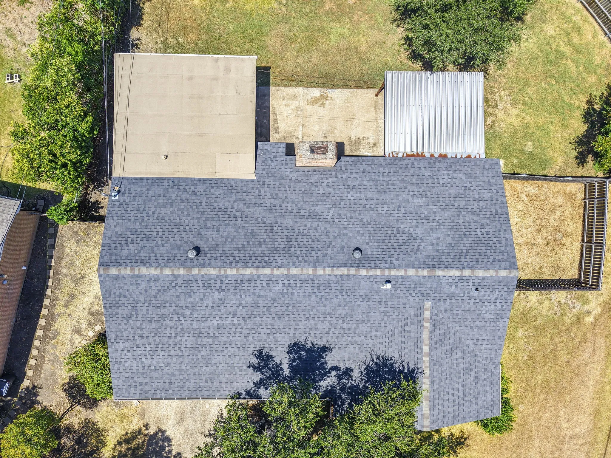 Asphalt shingle roof, flat roof extension, concrete slab, and a corrugated metal structure