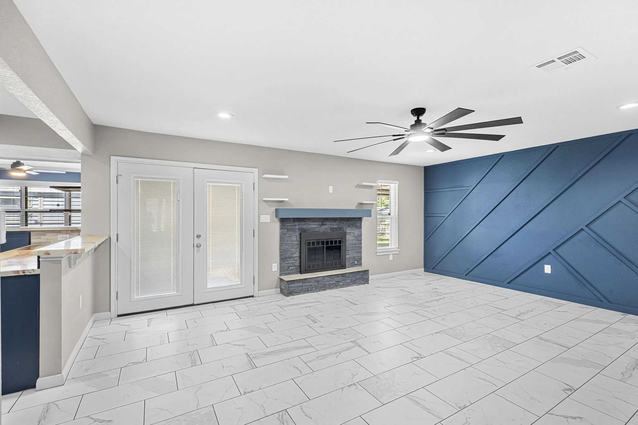 Expansive room featuring large format tile flooring, a fireplace with a stone surround, a modern ceiling fan, and a decorative accent wall
