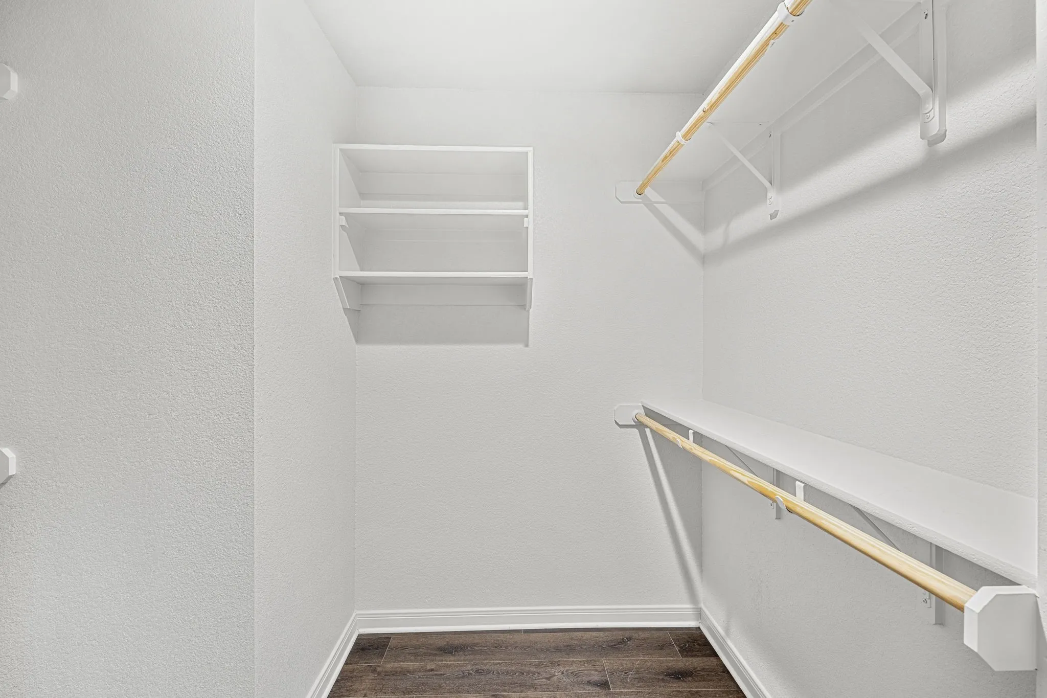 Built-in shelving, multiple hanging rods, and wood-finish flooring