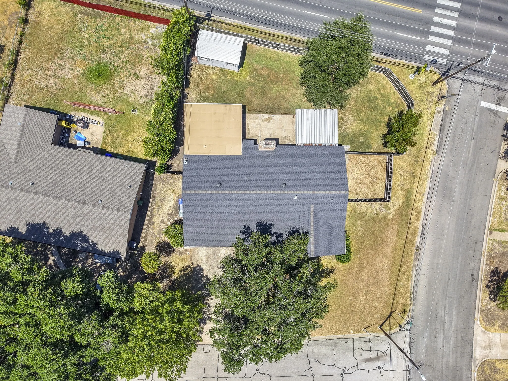 Property featuring a dark shingle roof, a light-colored flat roof section, and an adjacent corrugated metal roof structure