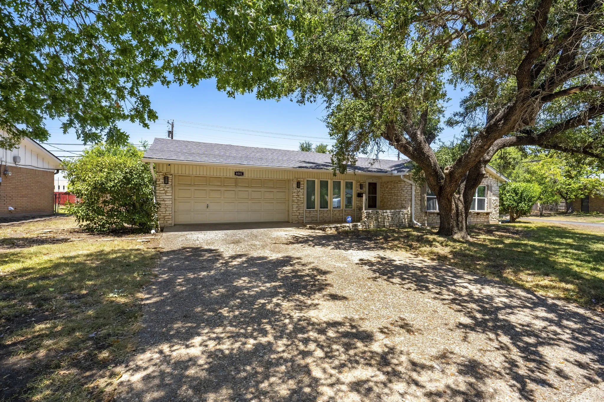 Stone veneer exterior, attached two-car garage, covered entry, and mature landscaping