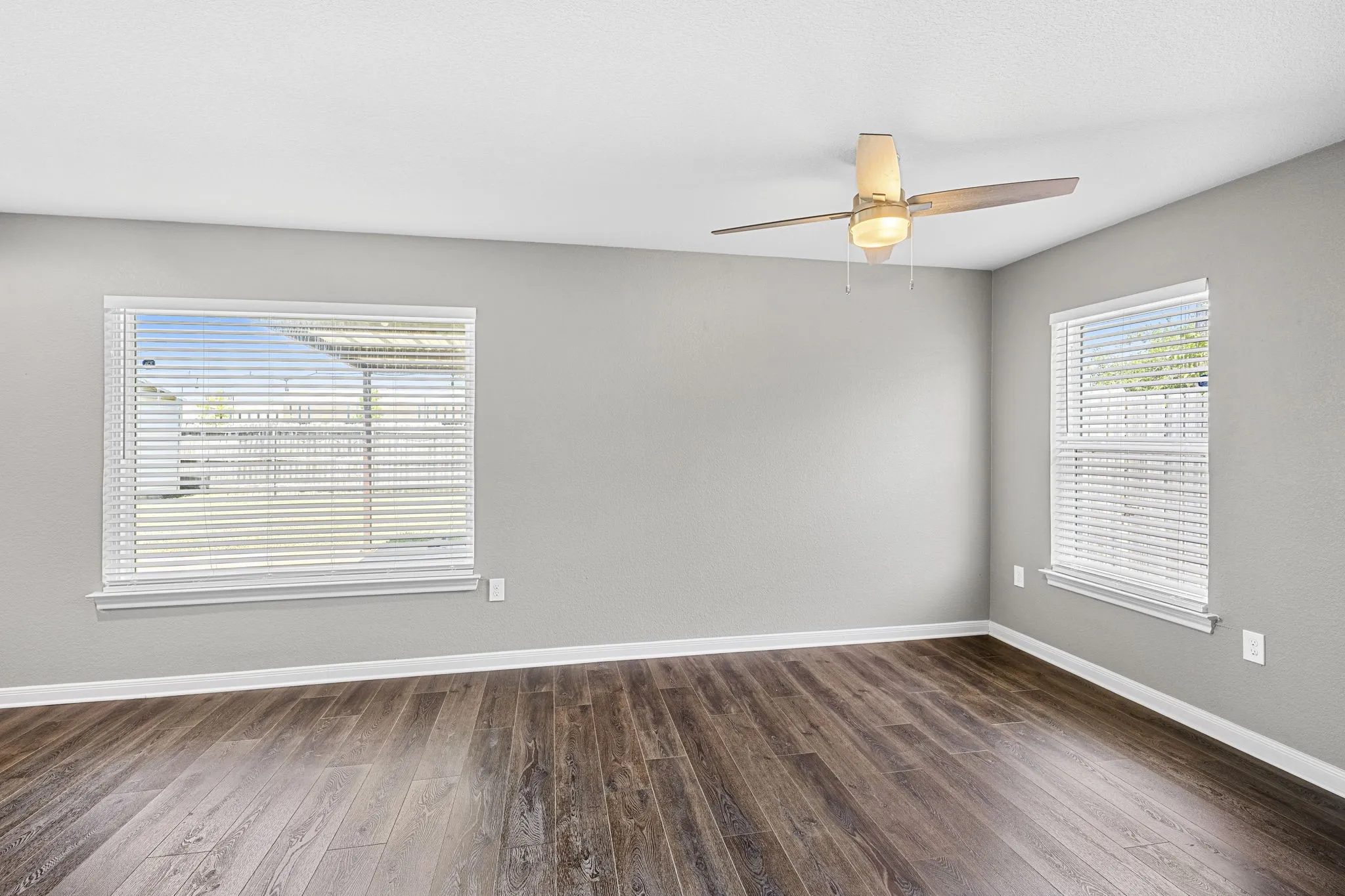 Wood-finish flooring, light gray wall tones, and multiple windows with horizontal blinds