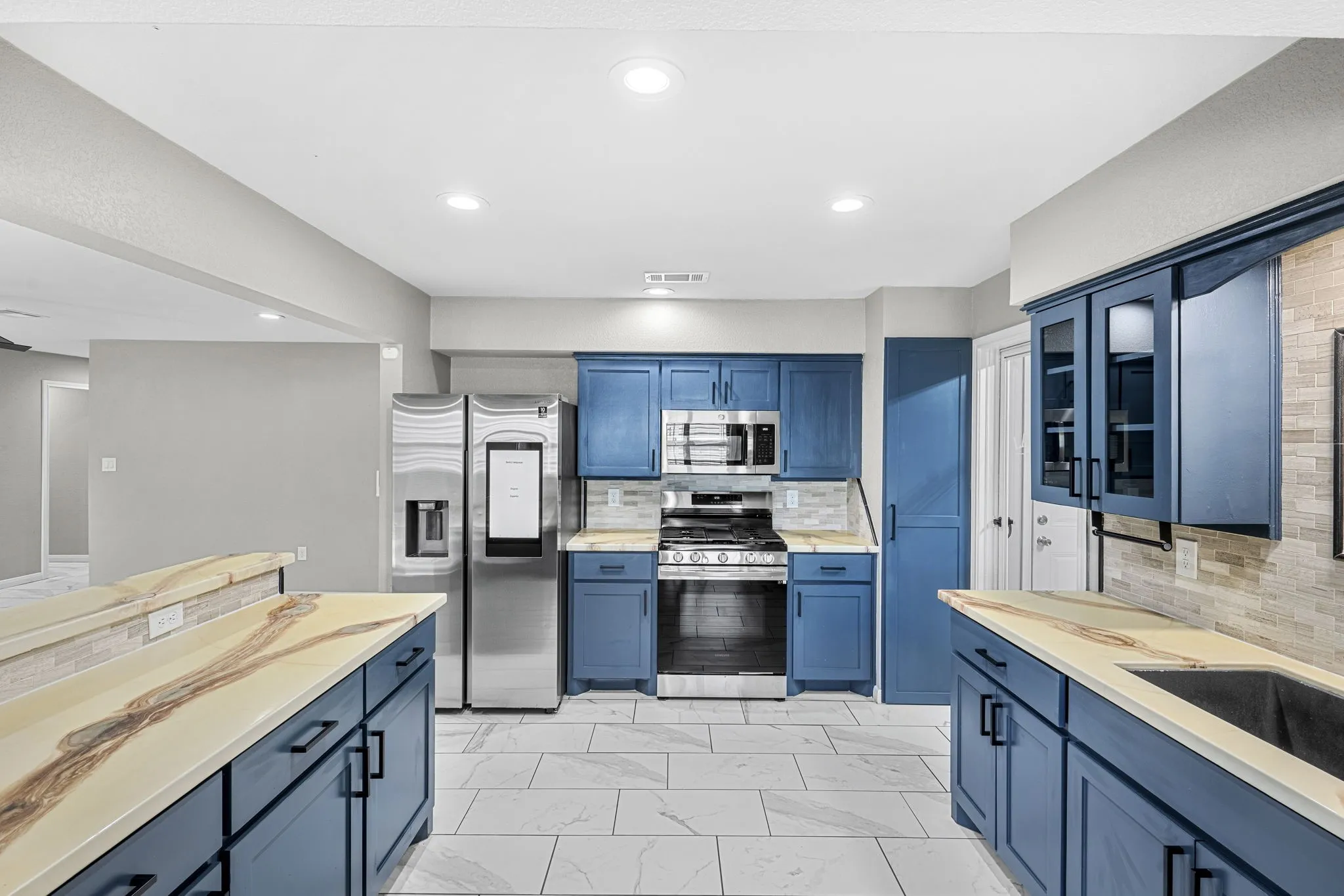 Kitchen featuring blue cabinetry, stainless steel appliances, light-toned countertops, and a tiled backsplash