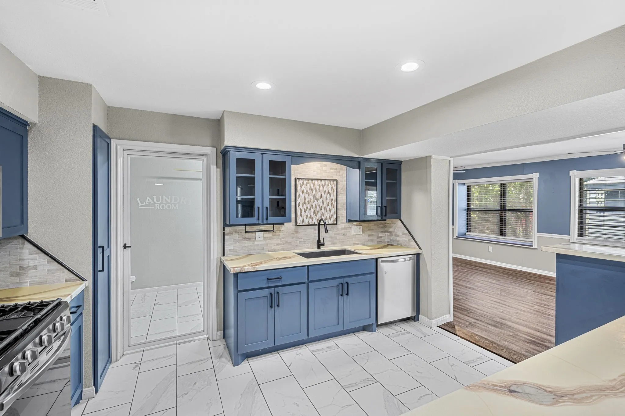 Kitchen featuring blue cabinetry, white tile flooring, light-toned countertops, a built-in dishwasher, and a glass-paneled door