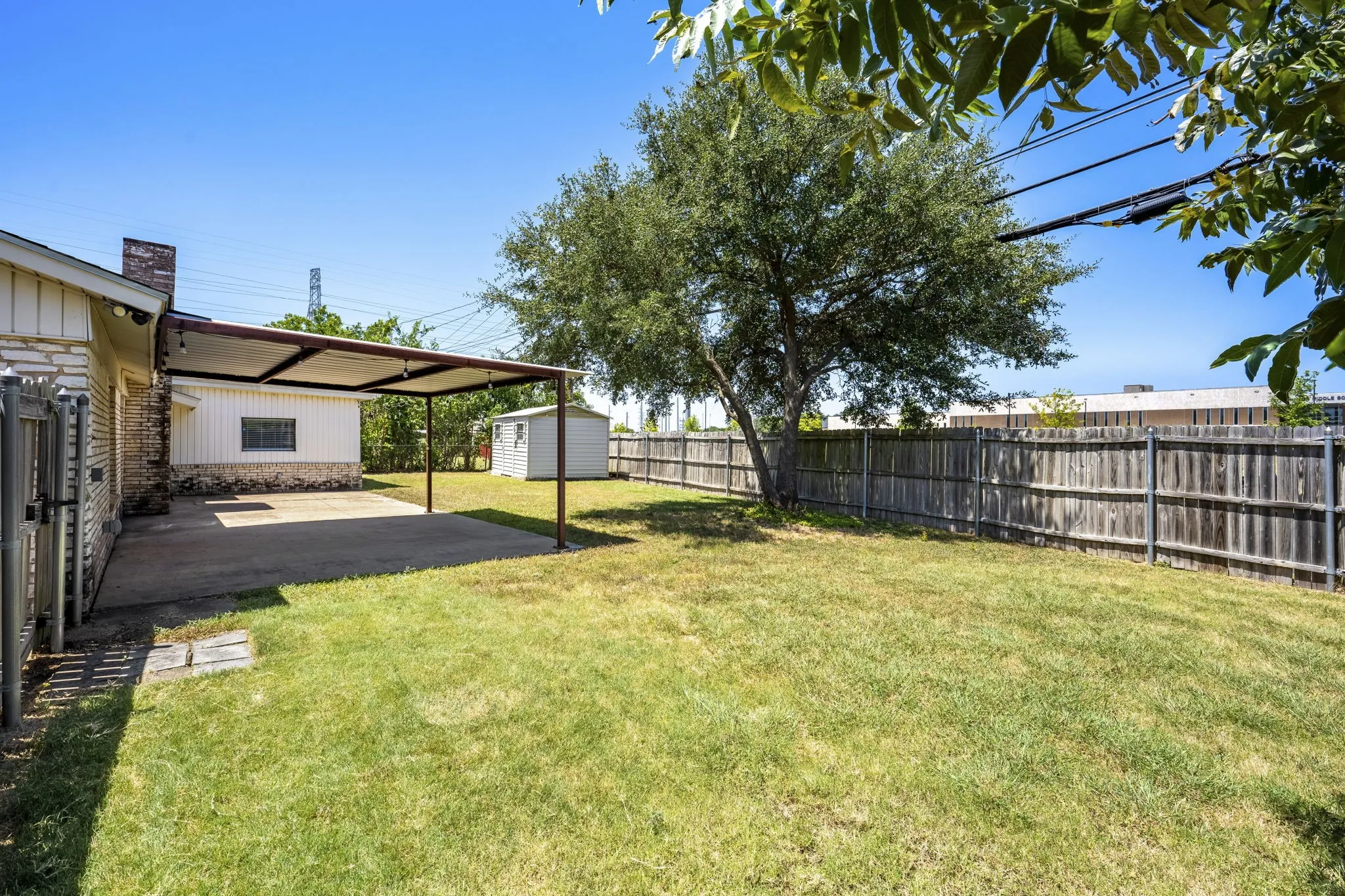 Expansive backyard featuring a covered patio, wood privacy fence, storage shed, and mature tree
