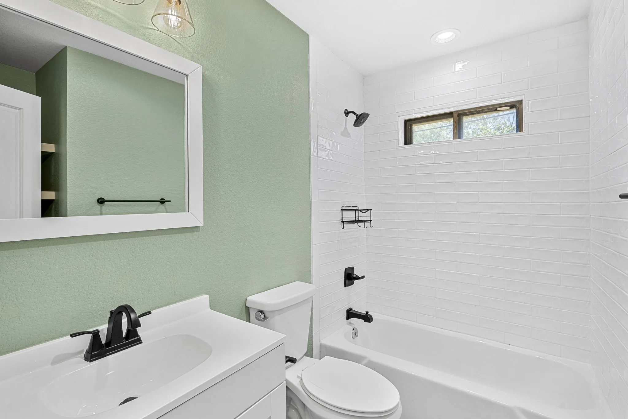White vanity with integrated sink, black hardware, framed mirror, built-in tub with subway tile surround, and recessed lighting