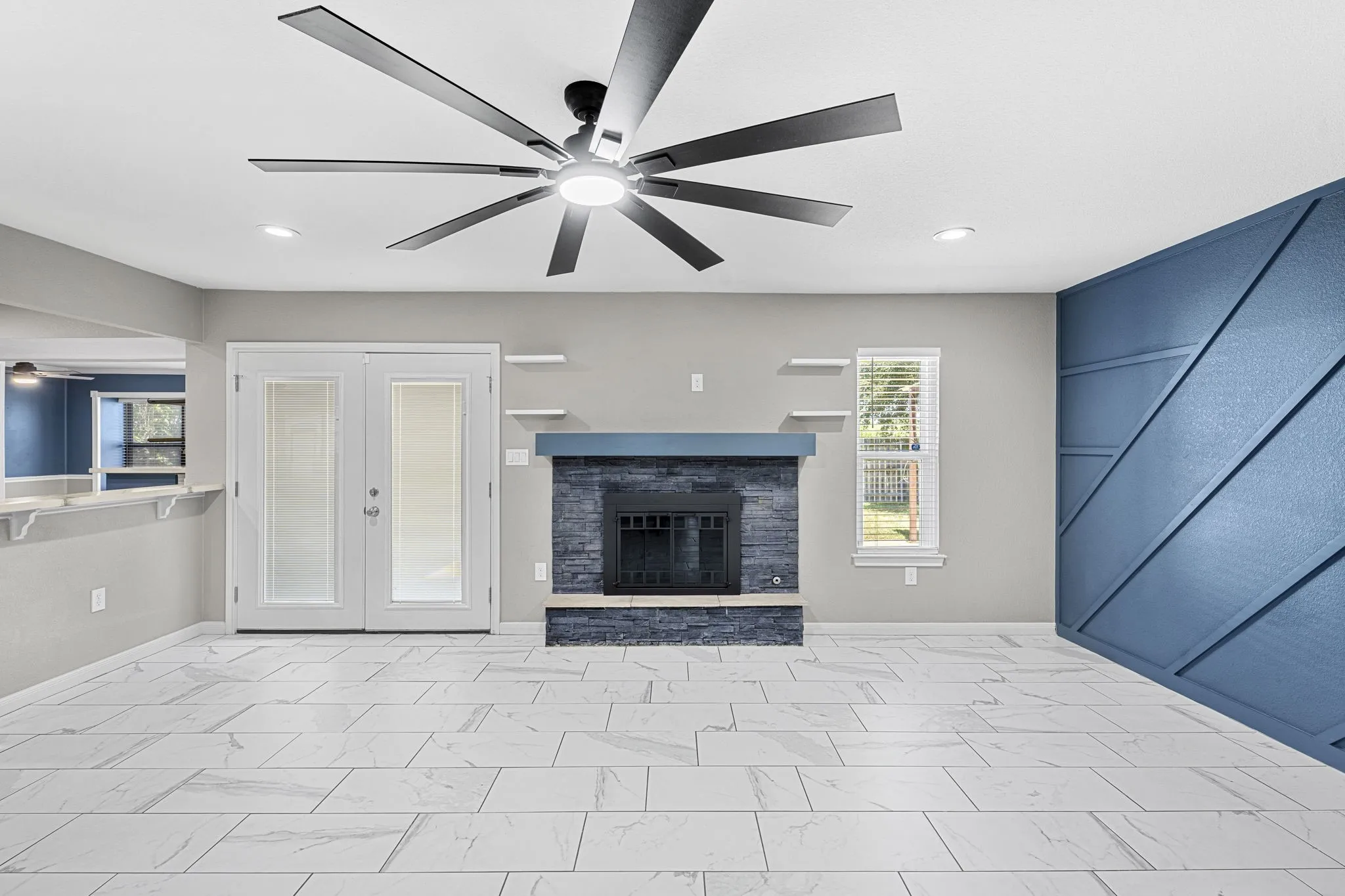 Spacious living area featuring large format tile flooring, a prominent fireplace with a dark stone surround and mantel, and a decorative accent wall