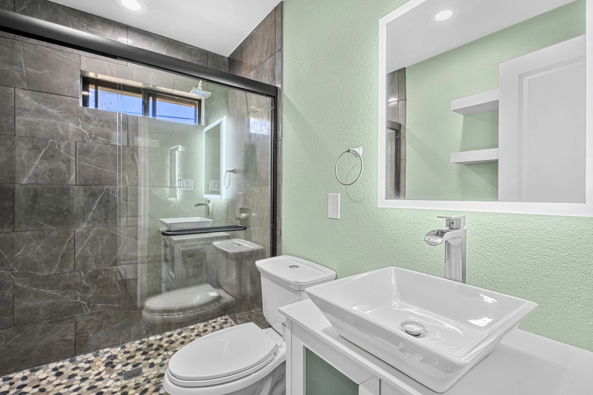 Glass-enclosed shower with dark stone-finish wall tile and pebble-finish floor