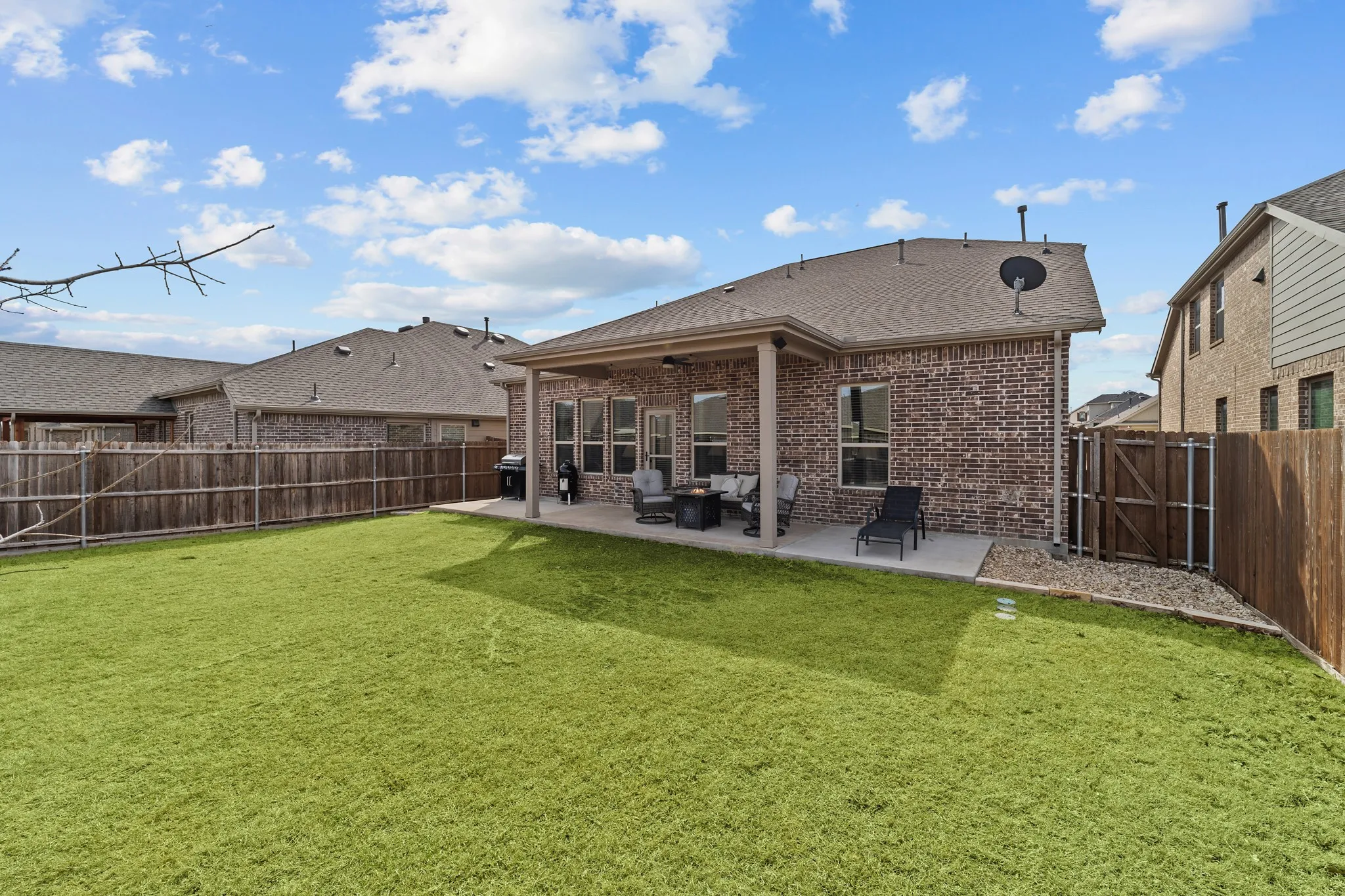 Spacious backyard featuring a covered concrete patio, brick exterior, wood privacy fencing, and a gravel accent area