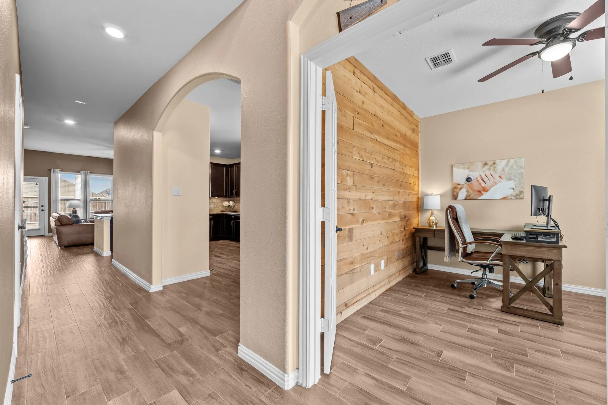 Open-concept layout featuring warm wood-finish tile flooring throughout, arched architectural details with white trim, and abundant recessed lighting