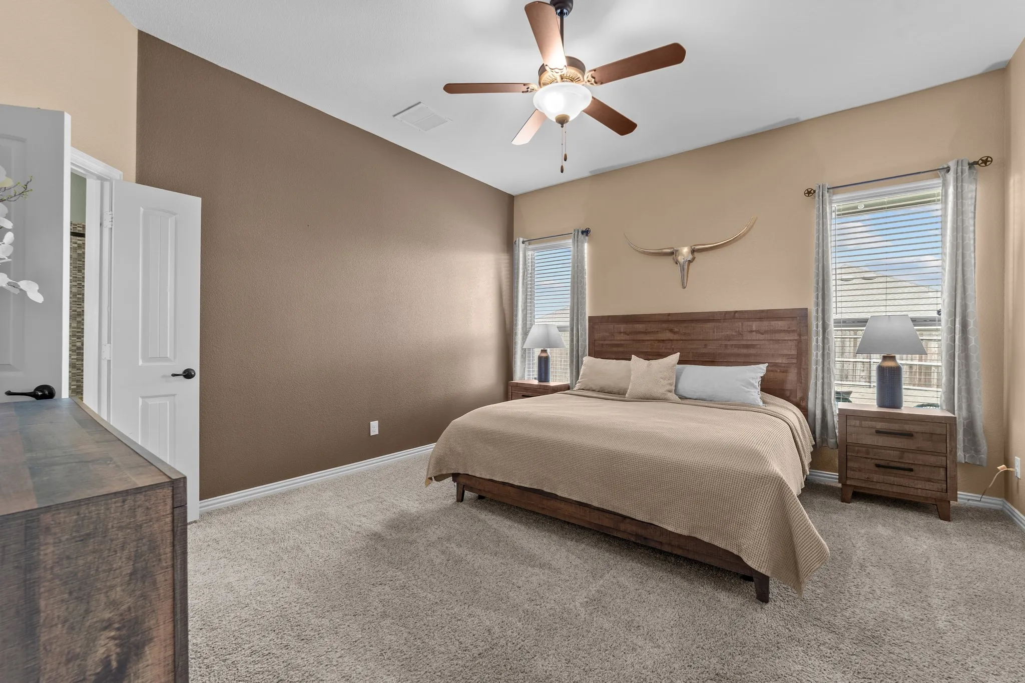 Primary Bedroom featuring neutral taupe walls, carpet flooring, ceiling fan with integrated lighting, multiple windows with horizontal blinds