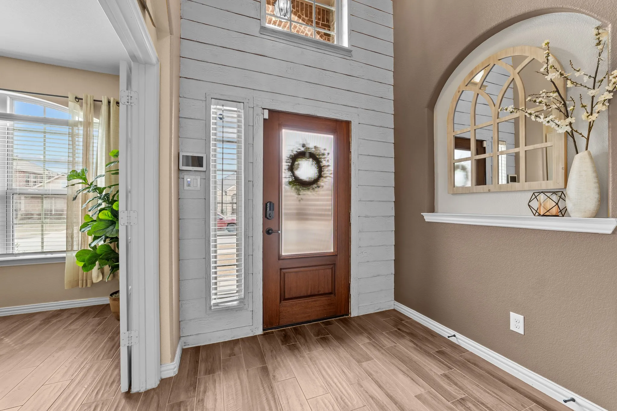 Welcoming foyer showcasing wood-finish plank tile flooring, soft taupe walls, and an arched mirror accent niche with built-in shelving