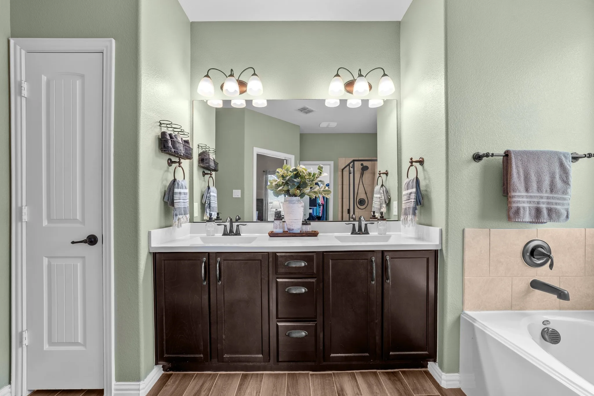 Dual-vanity master bathroom featuring dark wood cabinetry with ample storage, white quartz countertops, brushed nickel faucets, and dual illuminated mirrors