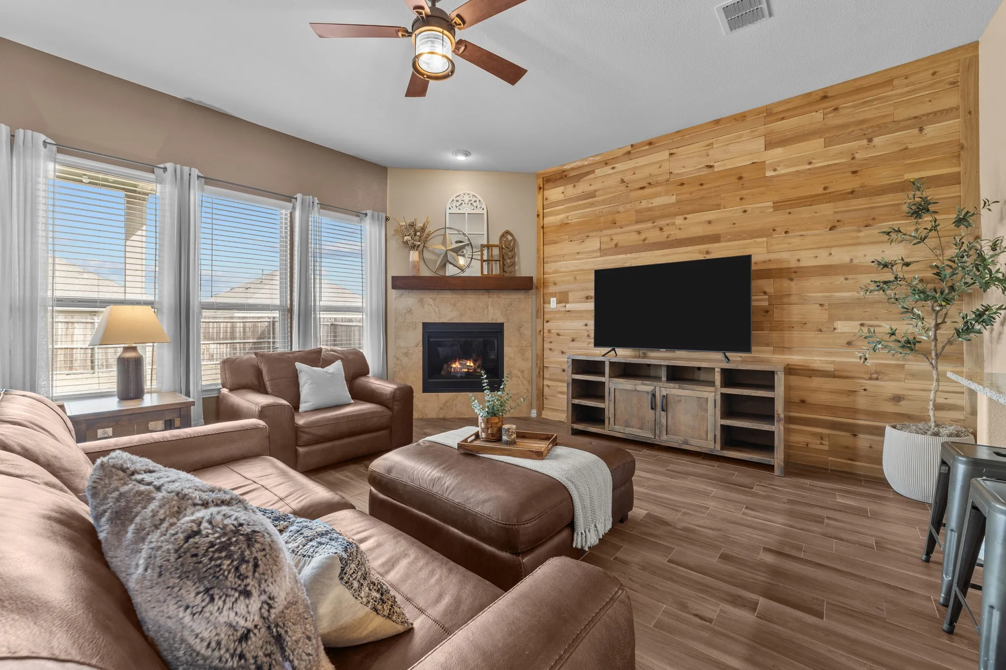 Spacious living room featuring a wood-paneled accent wall, wood-finish tile flooring, and a fireplace with decorative surround