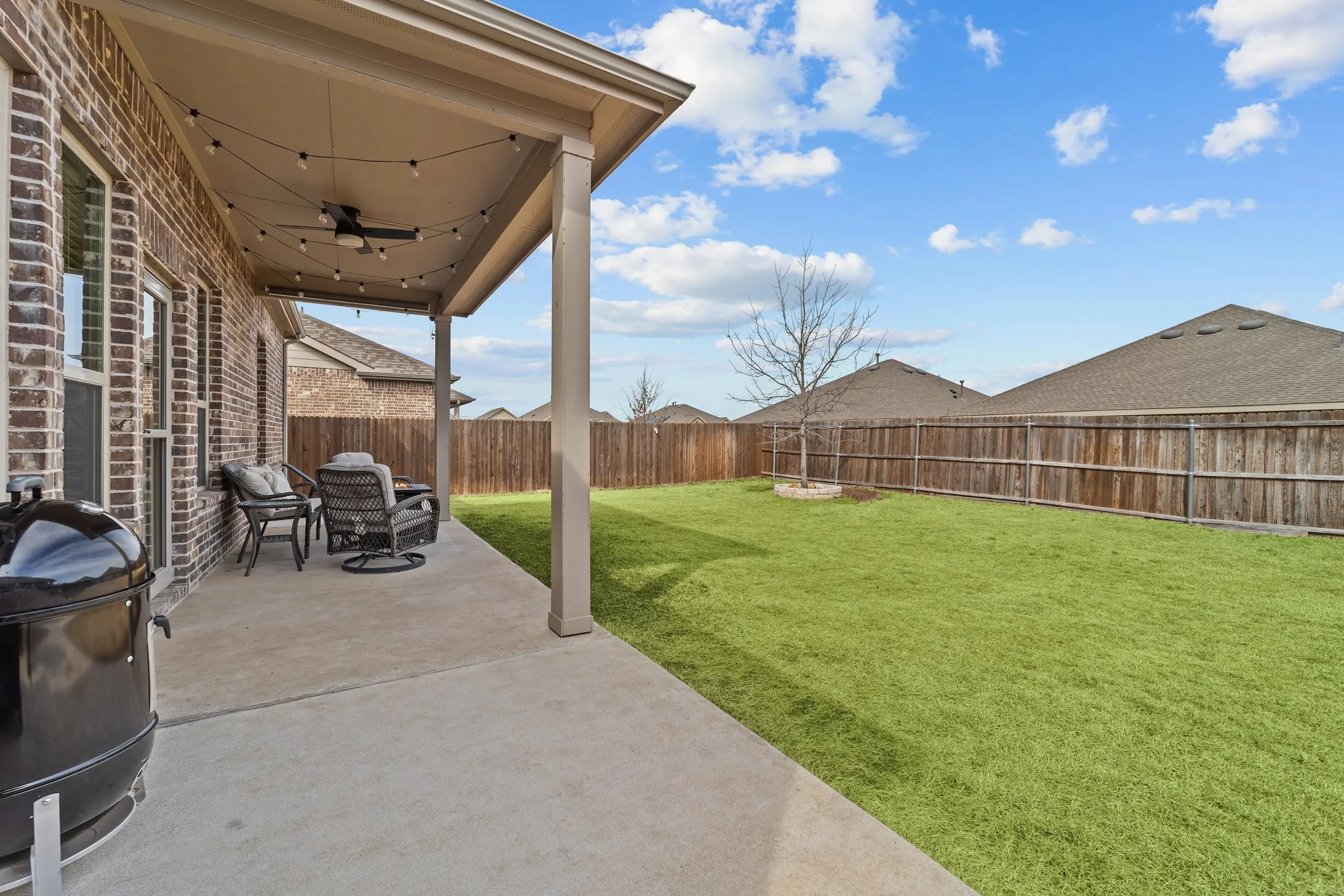 Expansive backyard featuring a manicured lawn, mature wooden privacy fencing, and defined landscaping