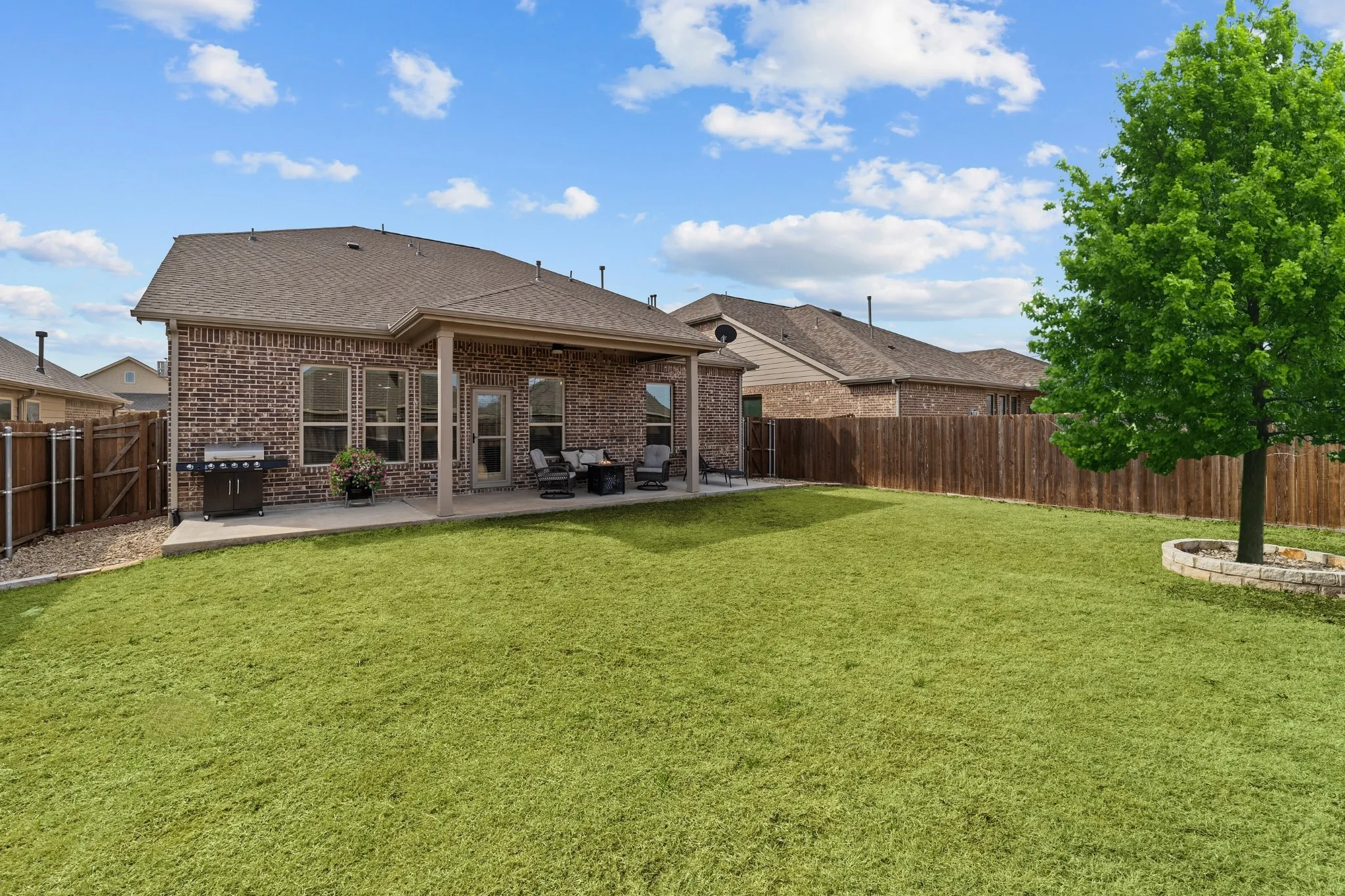 Expansive backyard with manicured lawn and mature landscaping, anchored by a large shade tree