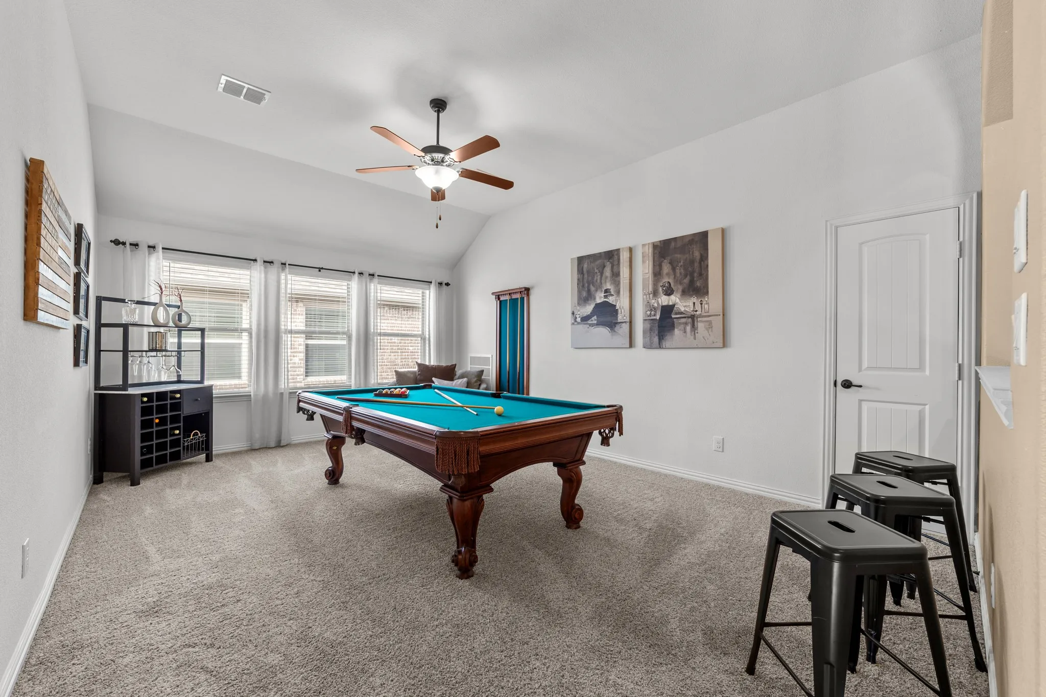 Spacious recreation room featuring neutral carpet flooring, a ceiling fan with integrated lighting, large windows with natural light, and white painted walls