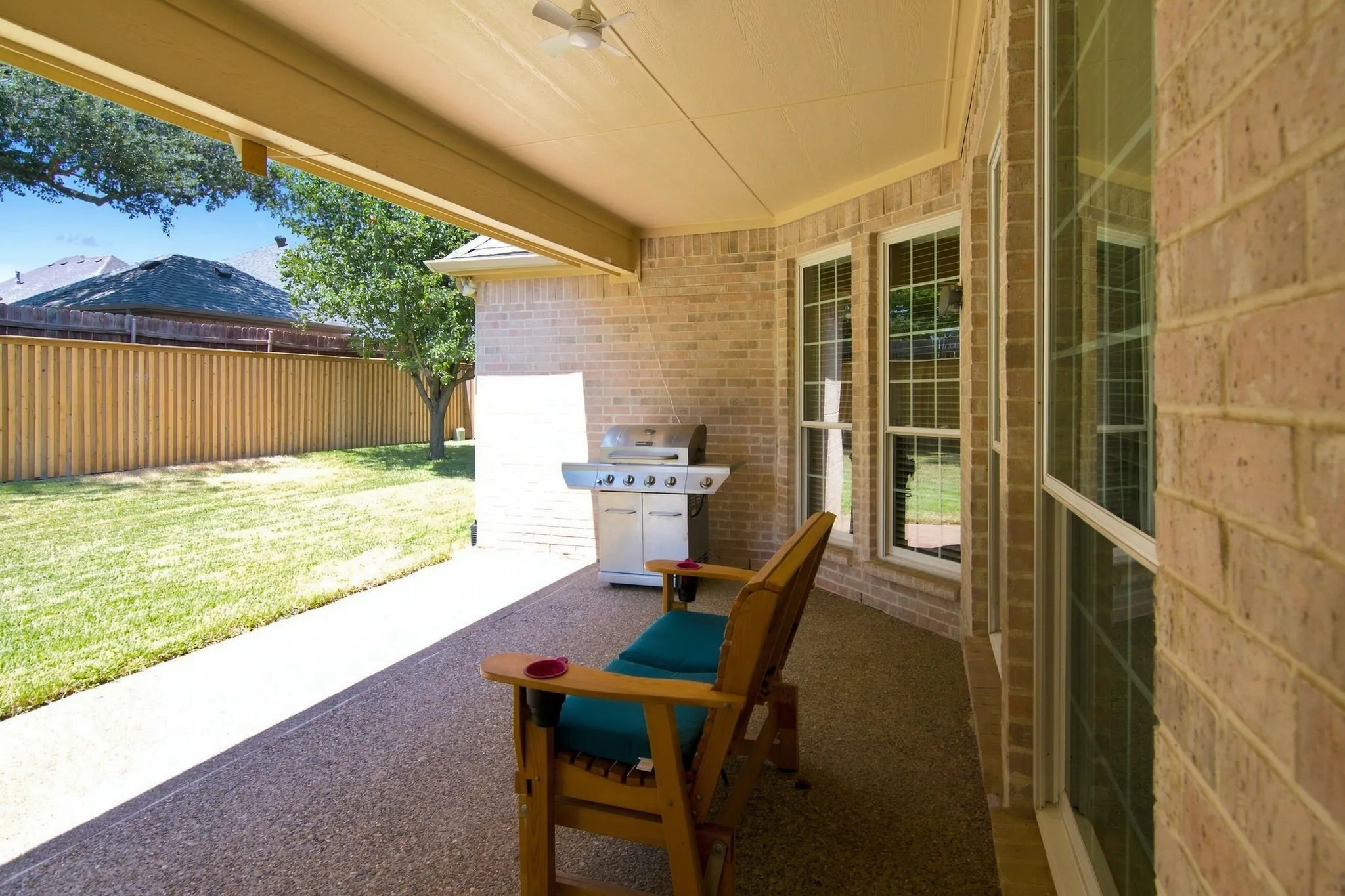 Covered patio with a ceiling fan, brick exterior, multiple windows, and a fenced backyard