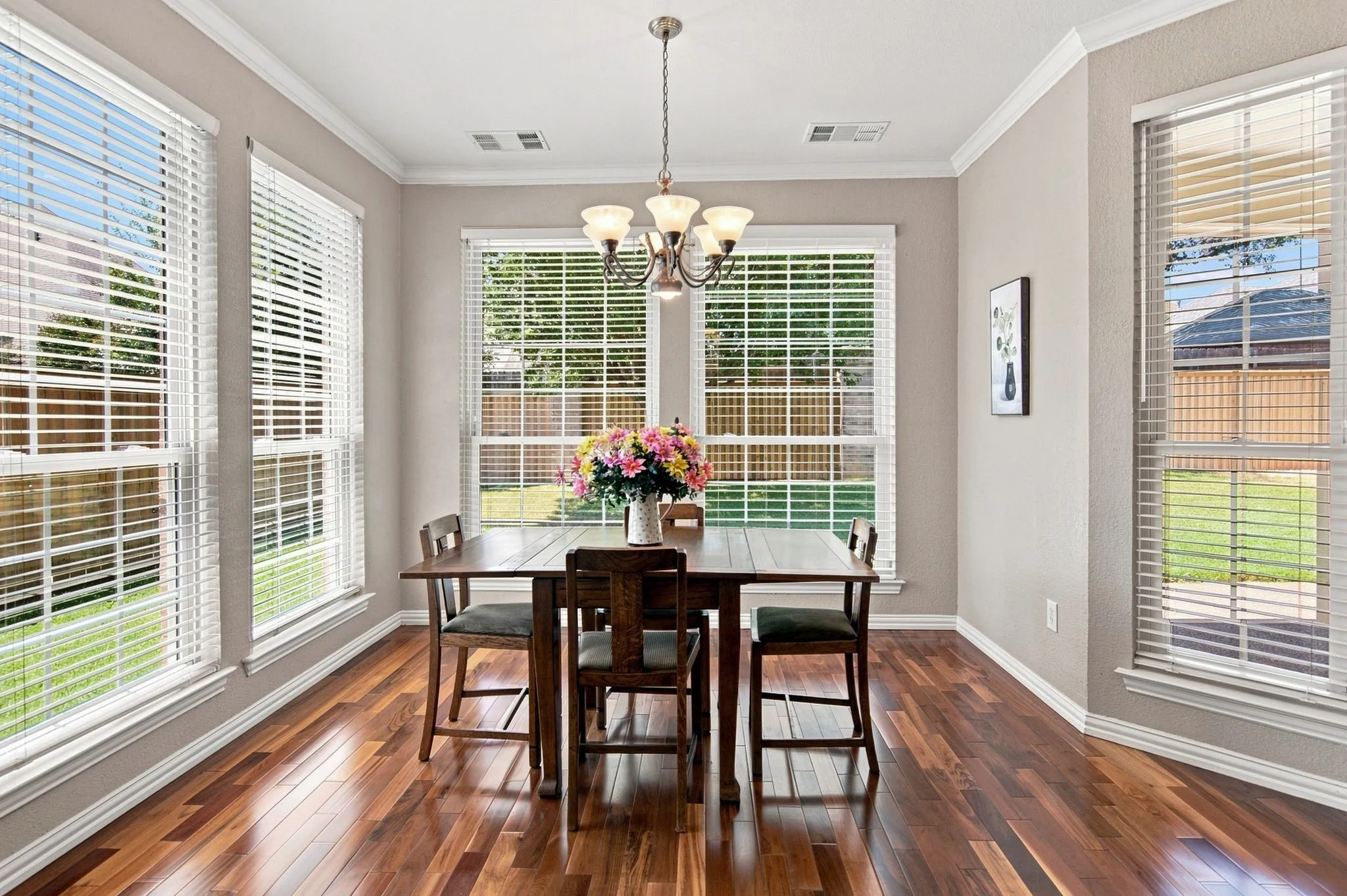 Hardwood flooring, multiple windows with blinds, crown molding, and a built-in chandelier with frosted glass shades