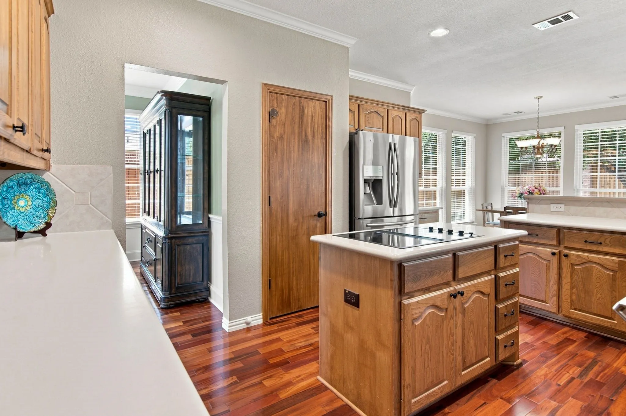 Kitchen featuring wood-finish flooring, stainless steel appliances, a center island with a cooktop, and light-toned cabinetry