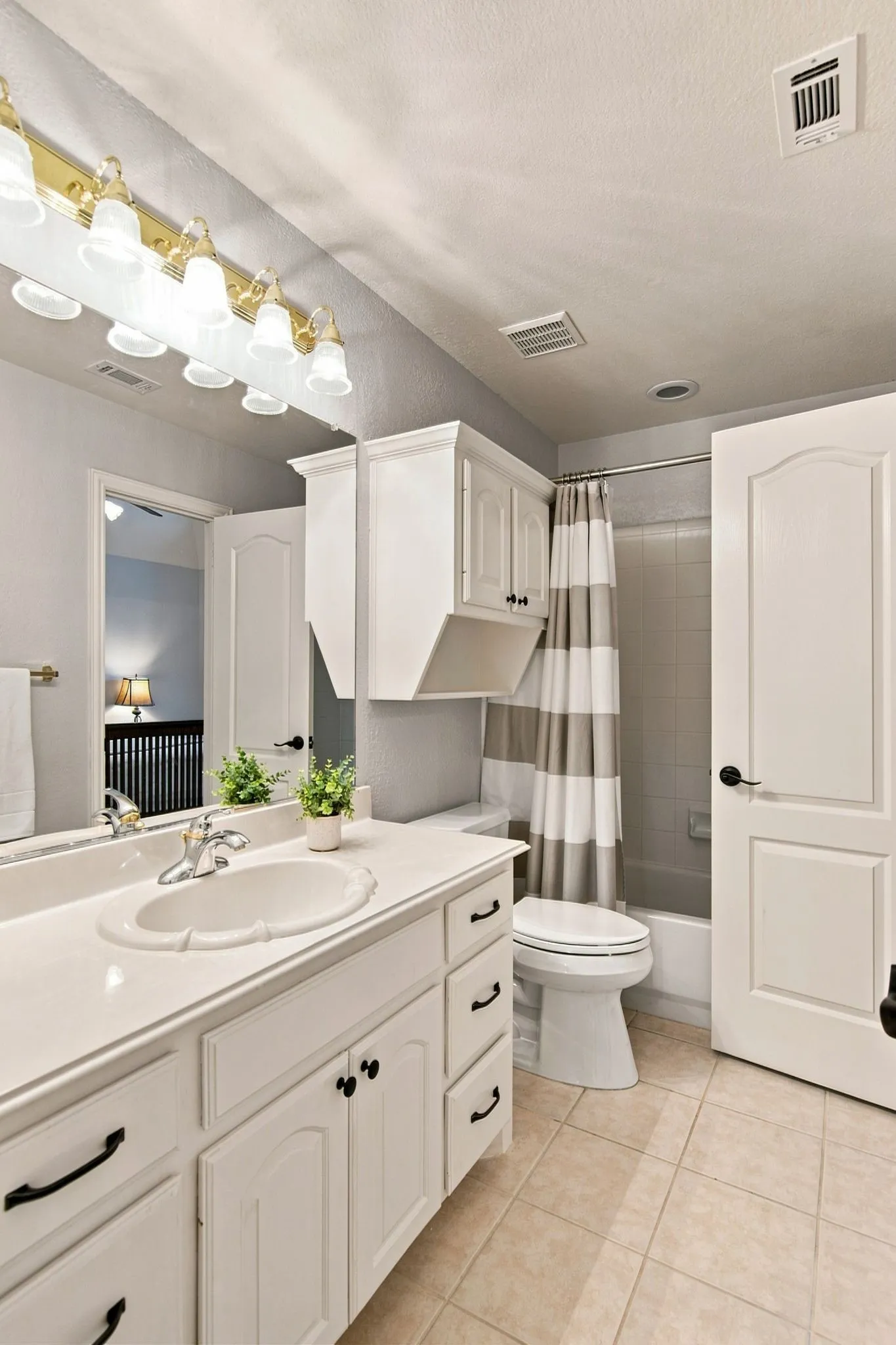 Spa-inspired bathroom featuring white cabinetry with black hardware, a wide vanity with dual sink basins, and tile flooring