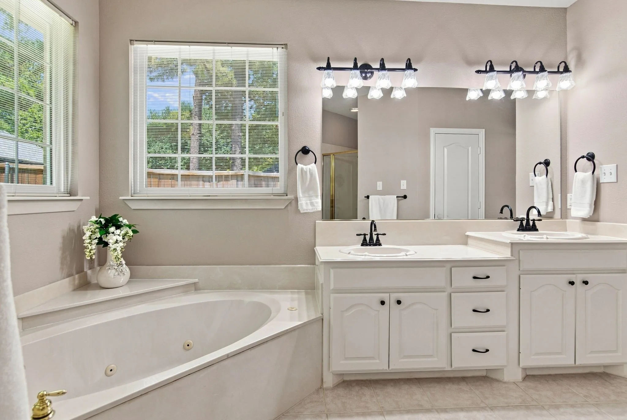 Spa-inspired primary bathroom featuring dual vanities with soft-close cabinetry, a soaking tub with deck-mounted fixtures, quartz countertops, and polished chrome faucetry