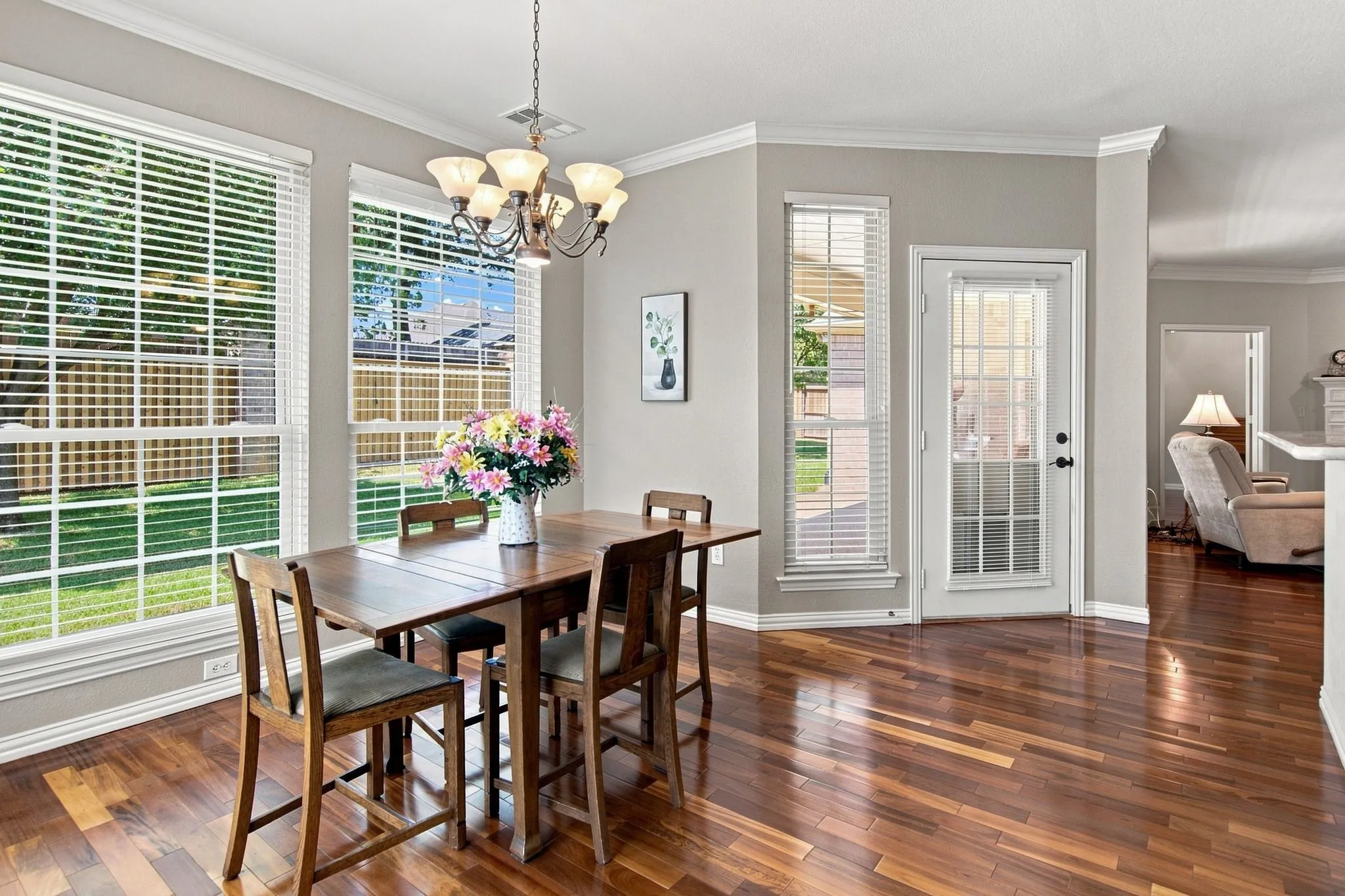 Bright dining space featuring hardwood flooring, a pendant light fixture, and expansive windows with plantation shutters overlooking the landscape