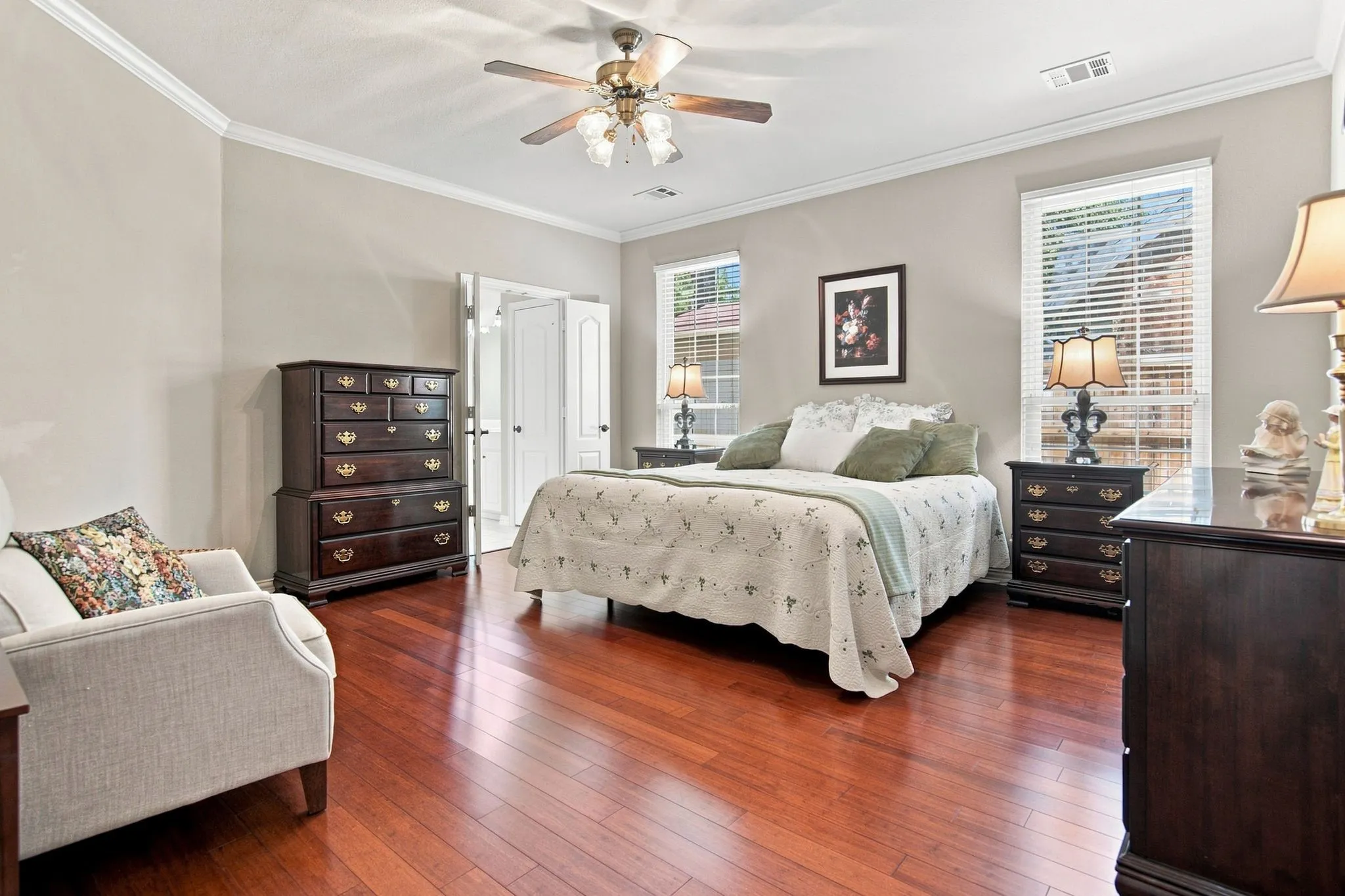 Spacious primary bedroom featuring hardwood flooring, a ceiling fan with integrated lighting, and abundant natural light from multiple windows