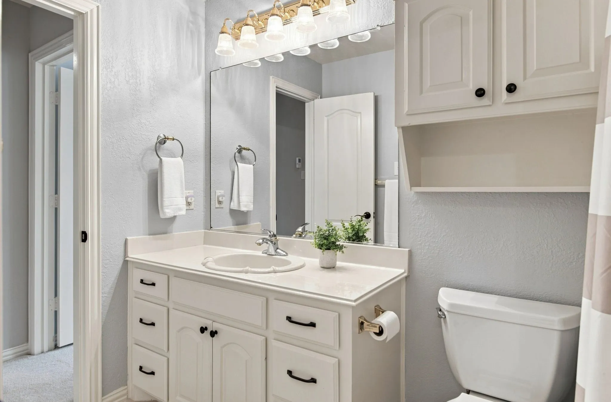 Bathroom featuring a vanity with an integrated sink, white cabinetry with black hardware, a wall-mounted mirror, and an overhead light fixture
