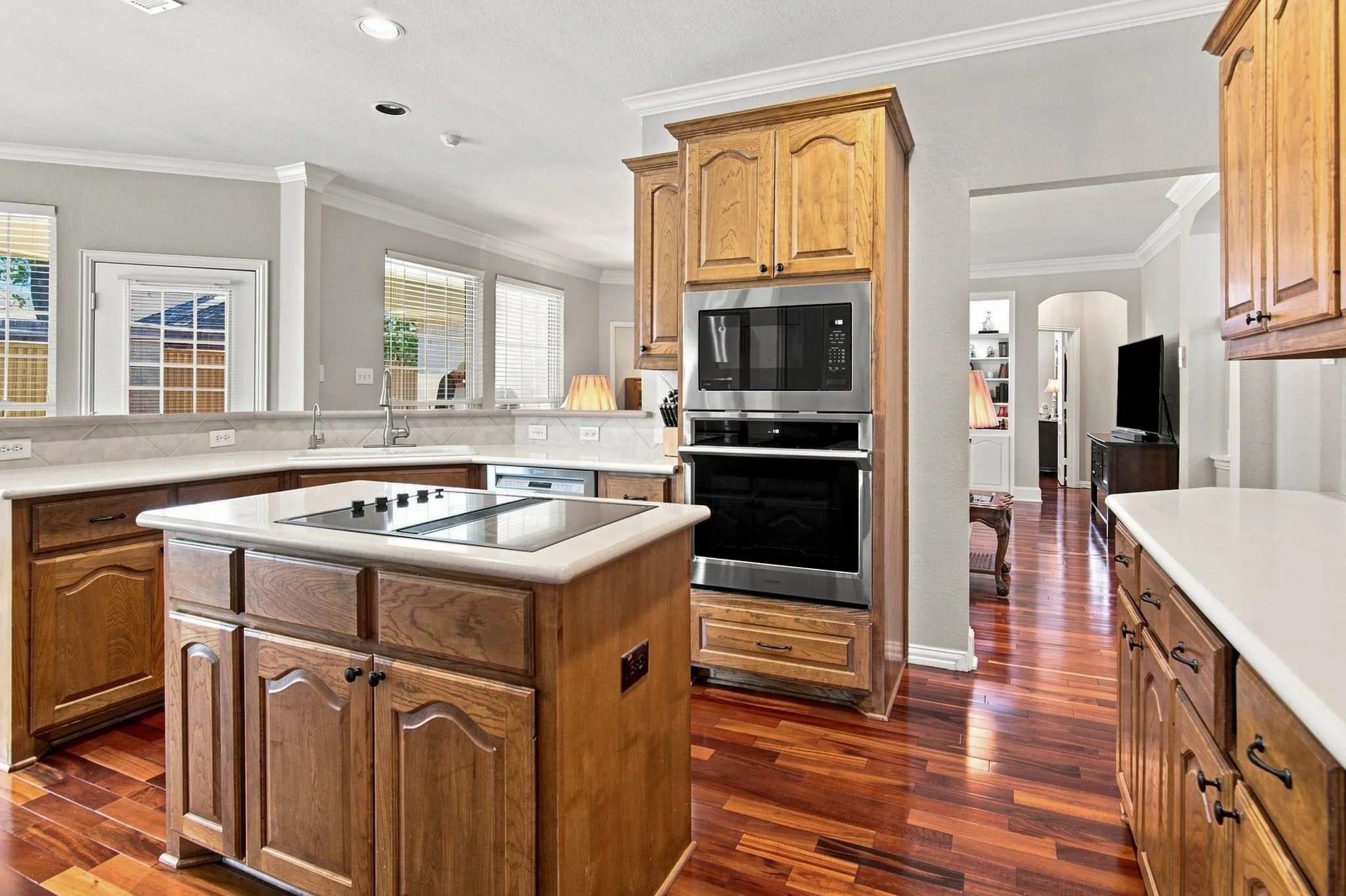 Gourmet kitchen featuring custom wood cabinetry, a substantial center island with prep space, stainless steel built-in appliances including double wall ovens, quartz countertops, and rich wood-finish flooring throughout the open layout