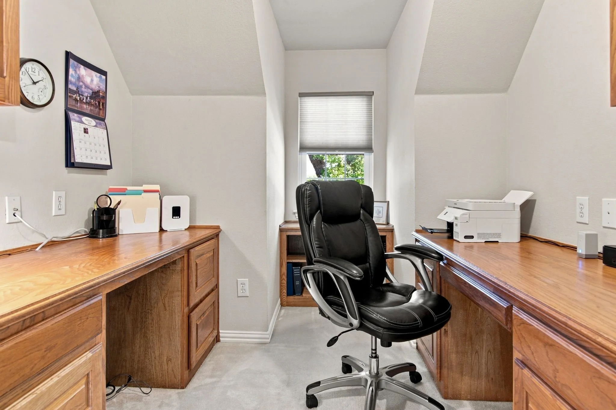 Dual-desk home office featuring rich wood-finish cabinetry, abundant natural light from a multi-pane window, vaulted ceiling with recessed lighting, and wall-mounted electrical outlets throughout