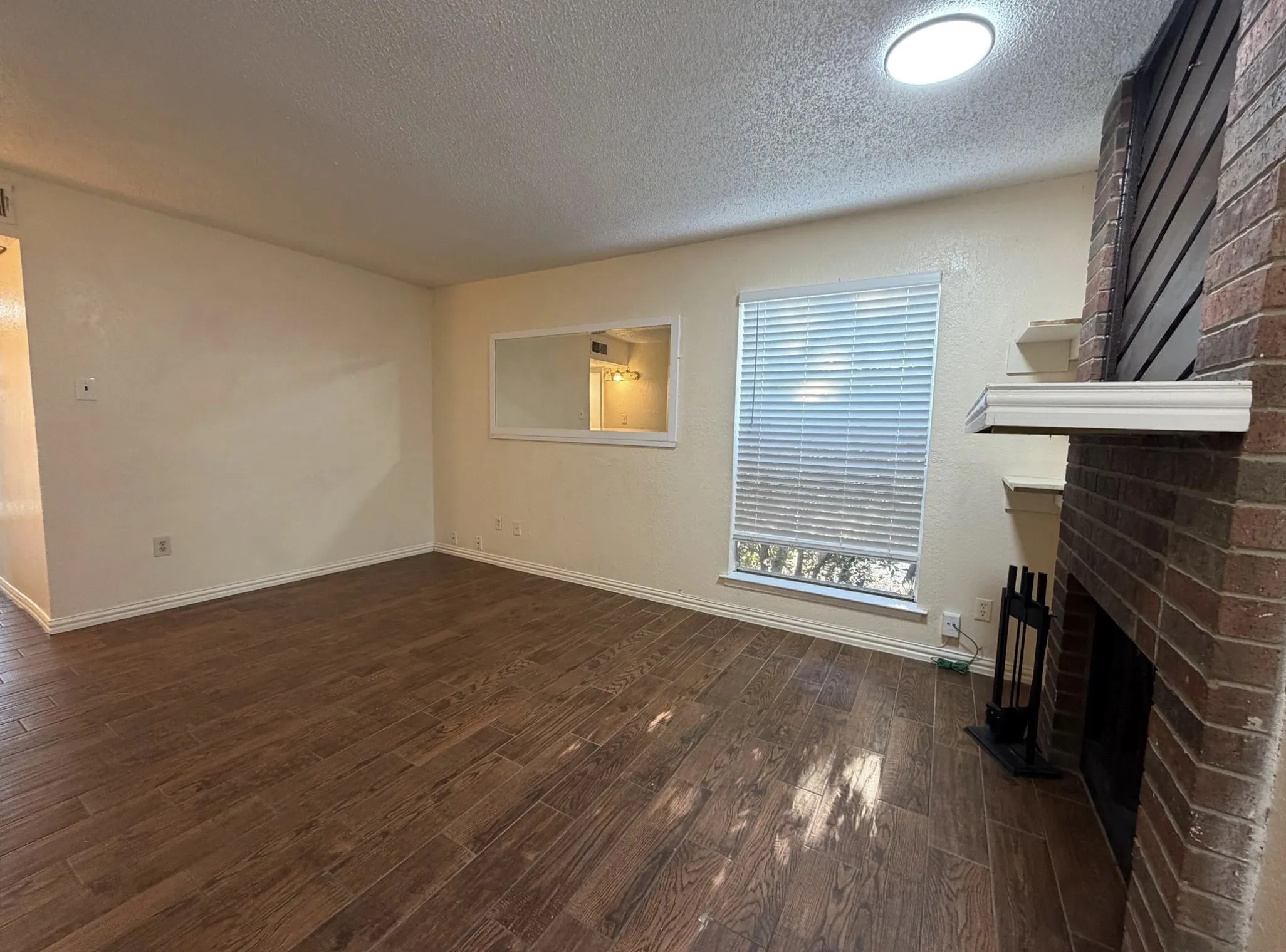 Wood-finish flooring, brick fireplace, built-in fireplace tools, recessed lighting, and a framed wall mirror