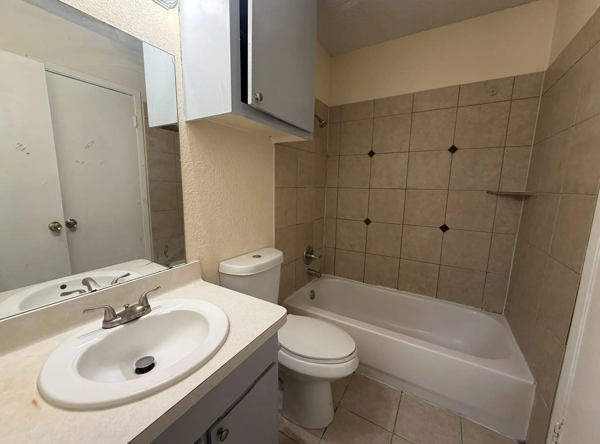 Bathroom featuring a single vanity with an integrated sink, wall-mounted mirror, built-in medicine cabinet, and a tiled shower-tub combination with decorative accent tiles