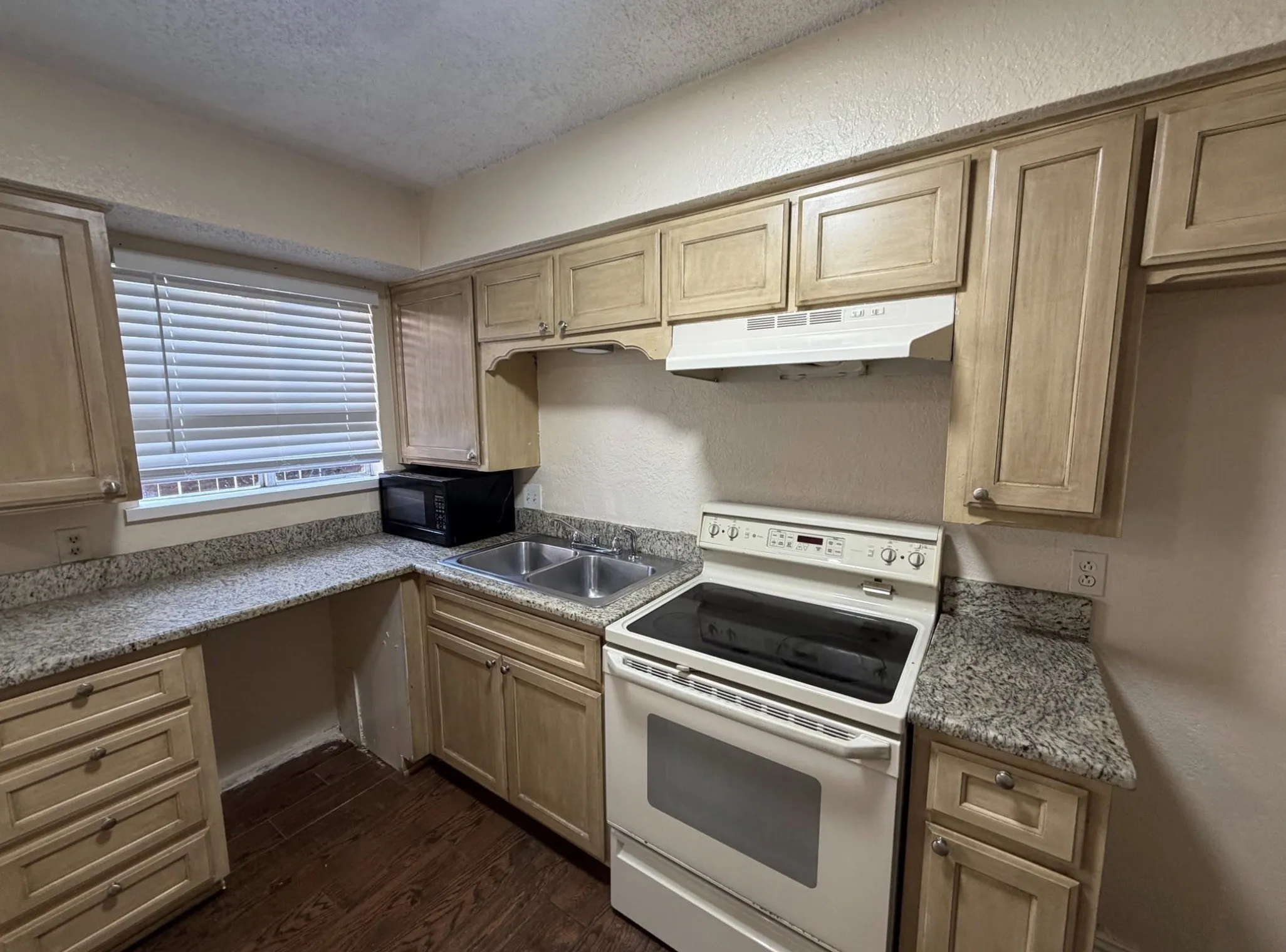Kitchen featuring wood-finish cabinetry, light-toned countertops, a stainless-steel double sink, and a white electric range with an overhead vent