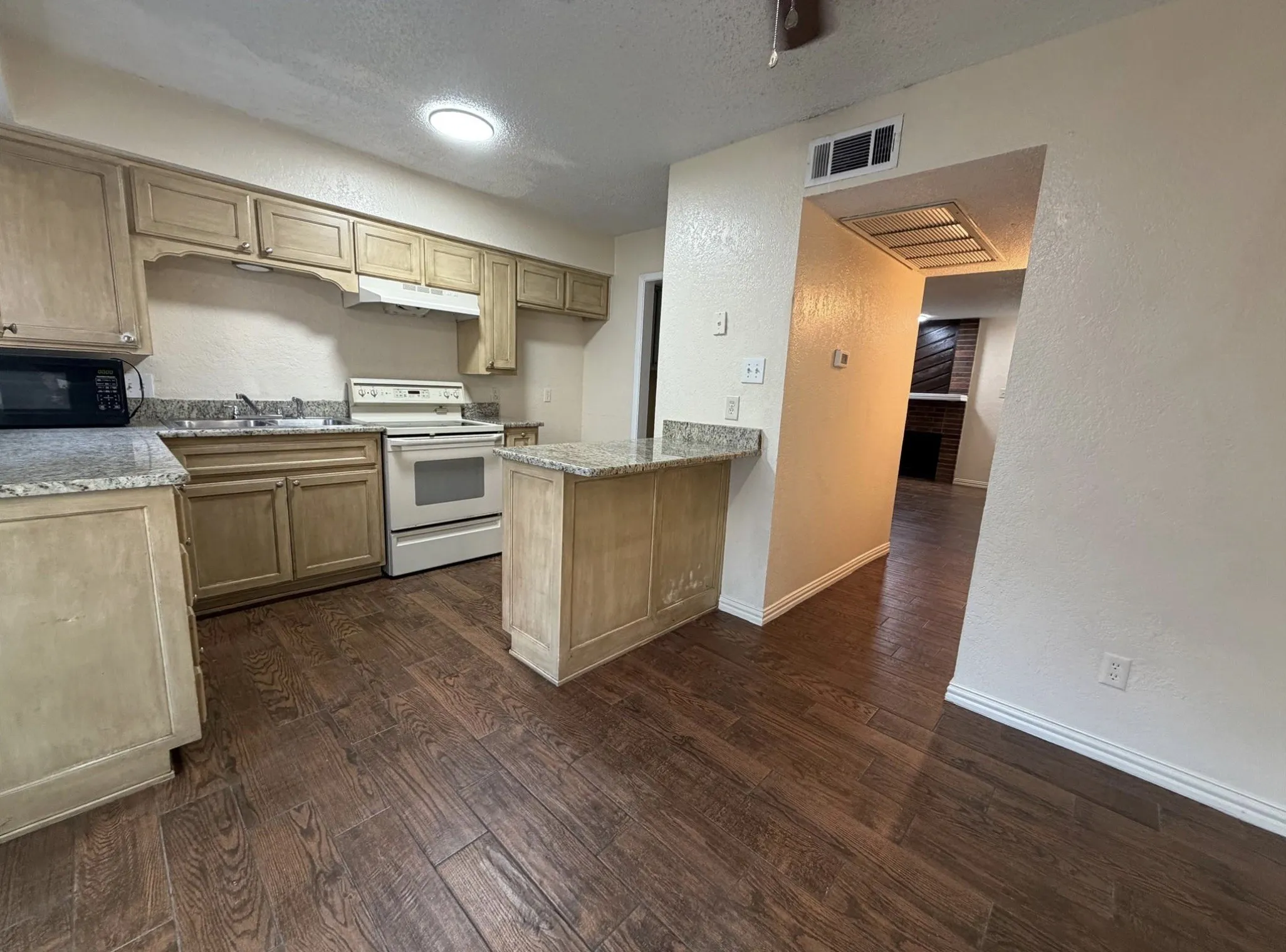Kitchen featuring wood-finish flooring, light wood cabinetry, stone-finish countertops, and a built-in breakfast bar